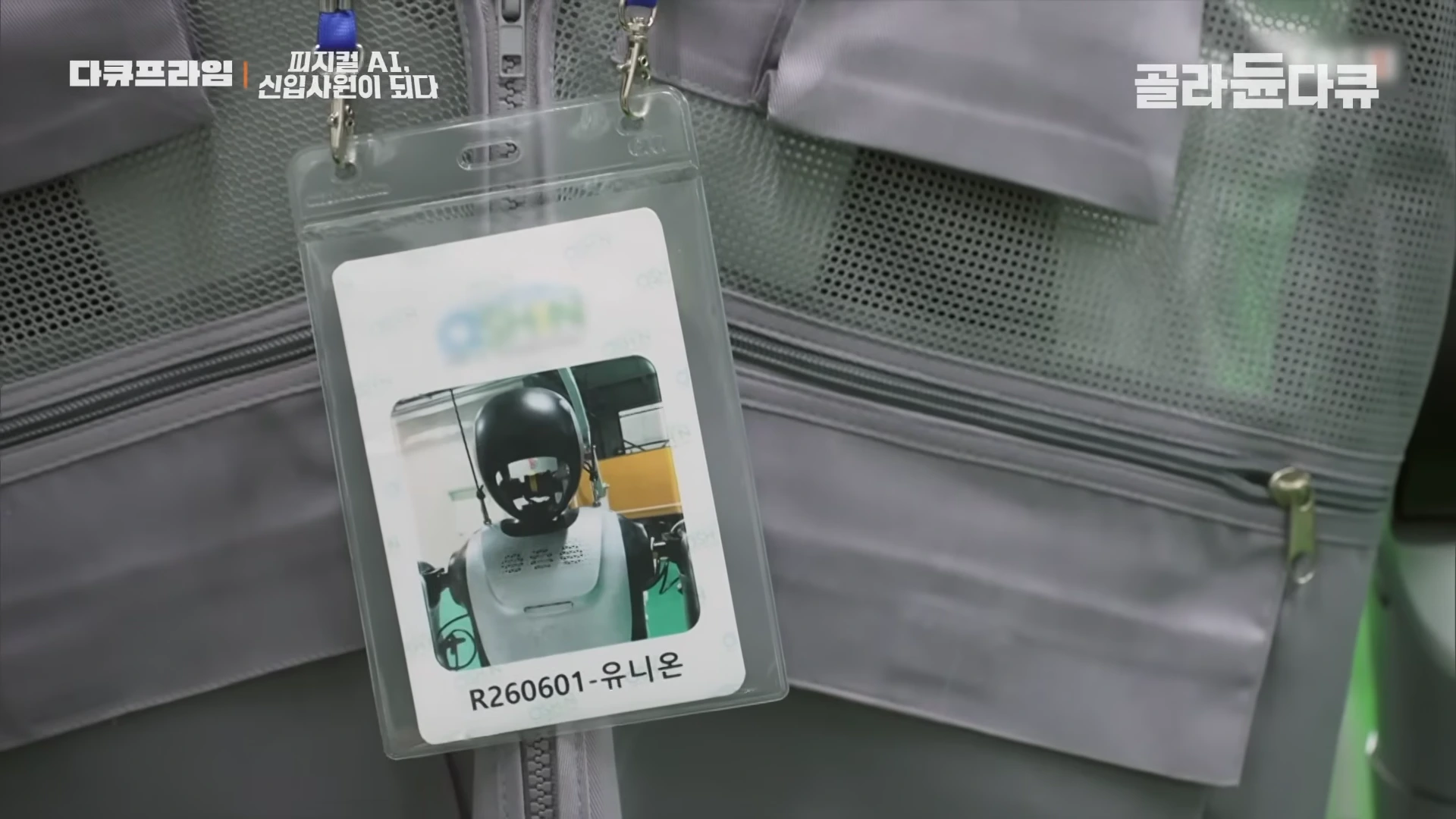로봇 사진과 이름이 적힌 투명한 사원증 케이스가 작업복 위에 걸려 있다.
