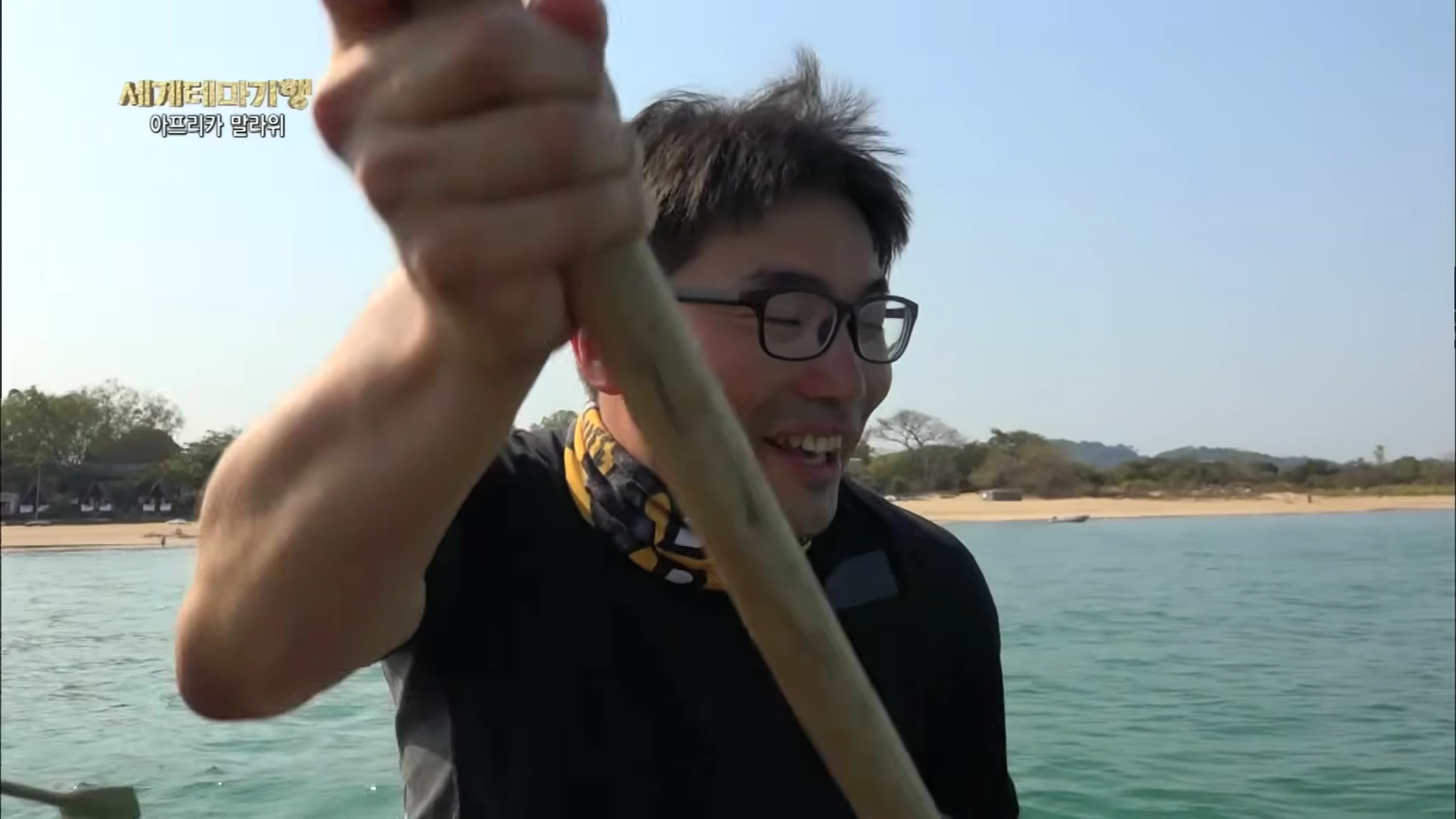 안경을 쓴 남성이 호수 위에서 노를 저으며 환하게 웃고 있는 모습