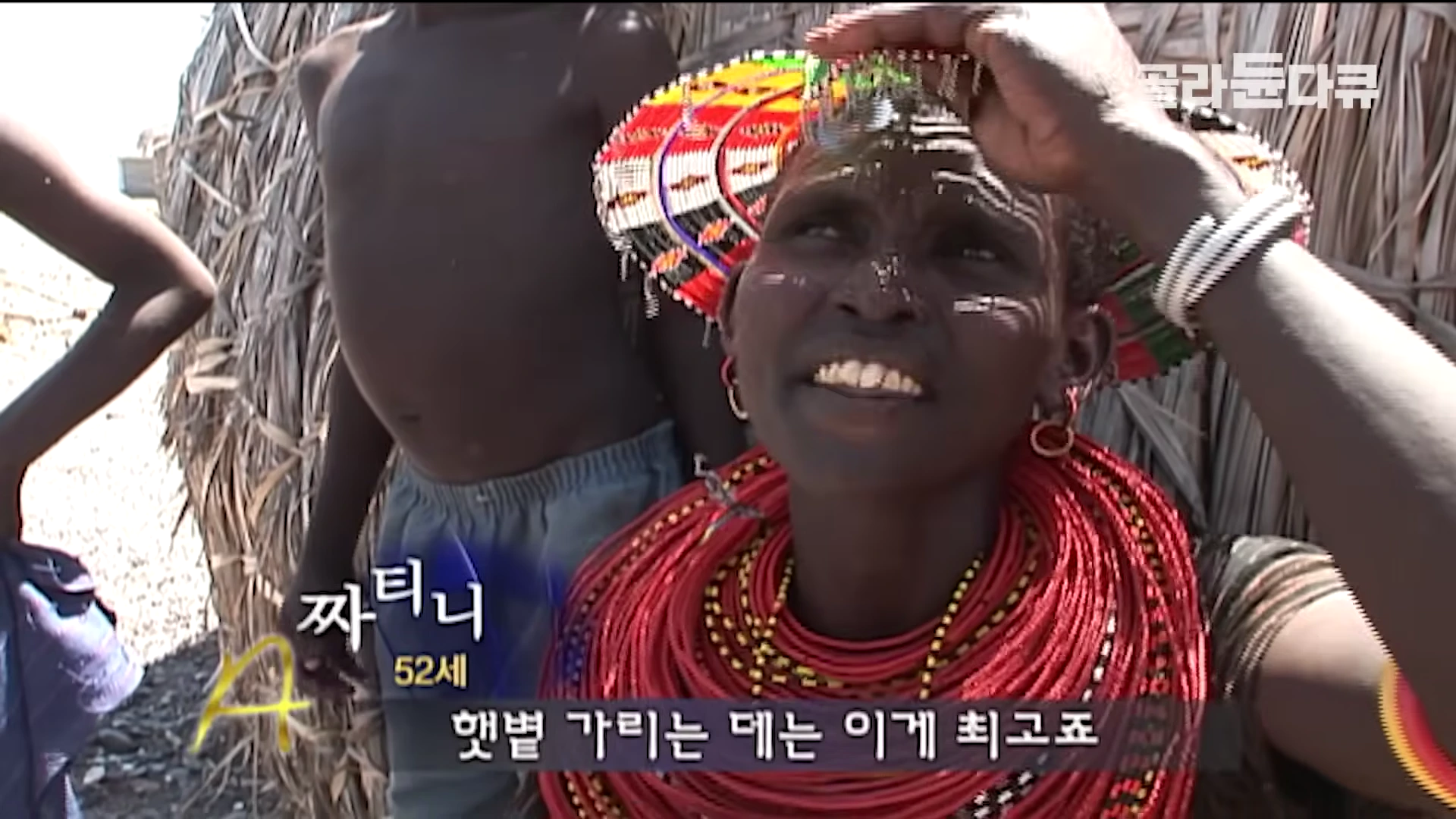 화려한 장신구를 머리에 쓴 엘모로족 여성이 뜨거운 햇볕을 가리고 있는 모습