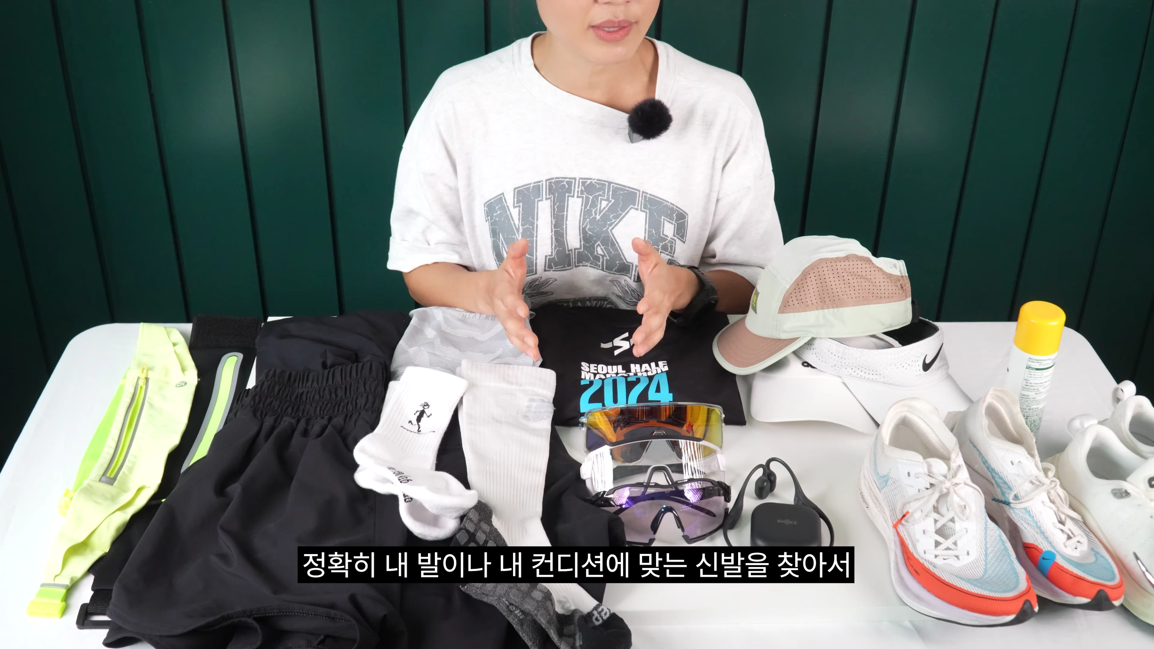 러닝 의류와 신발, 선글라스 등 다양한 러닝 장비가 놓인 테이블 앞에 앉아 설명하는 사람
