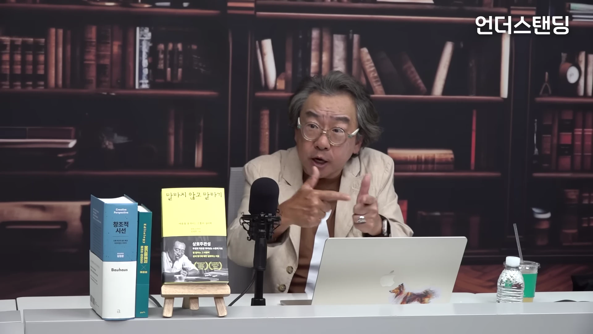 서재 배경의 스튜디오에서 중년 남성이 손짓하며 대화하는 모습