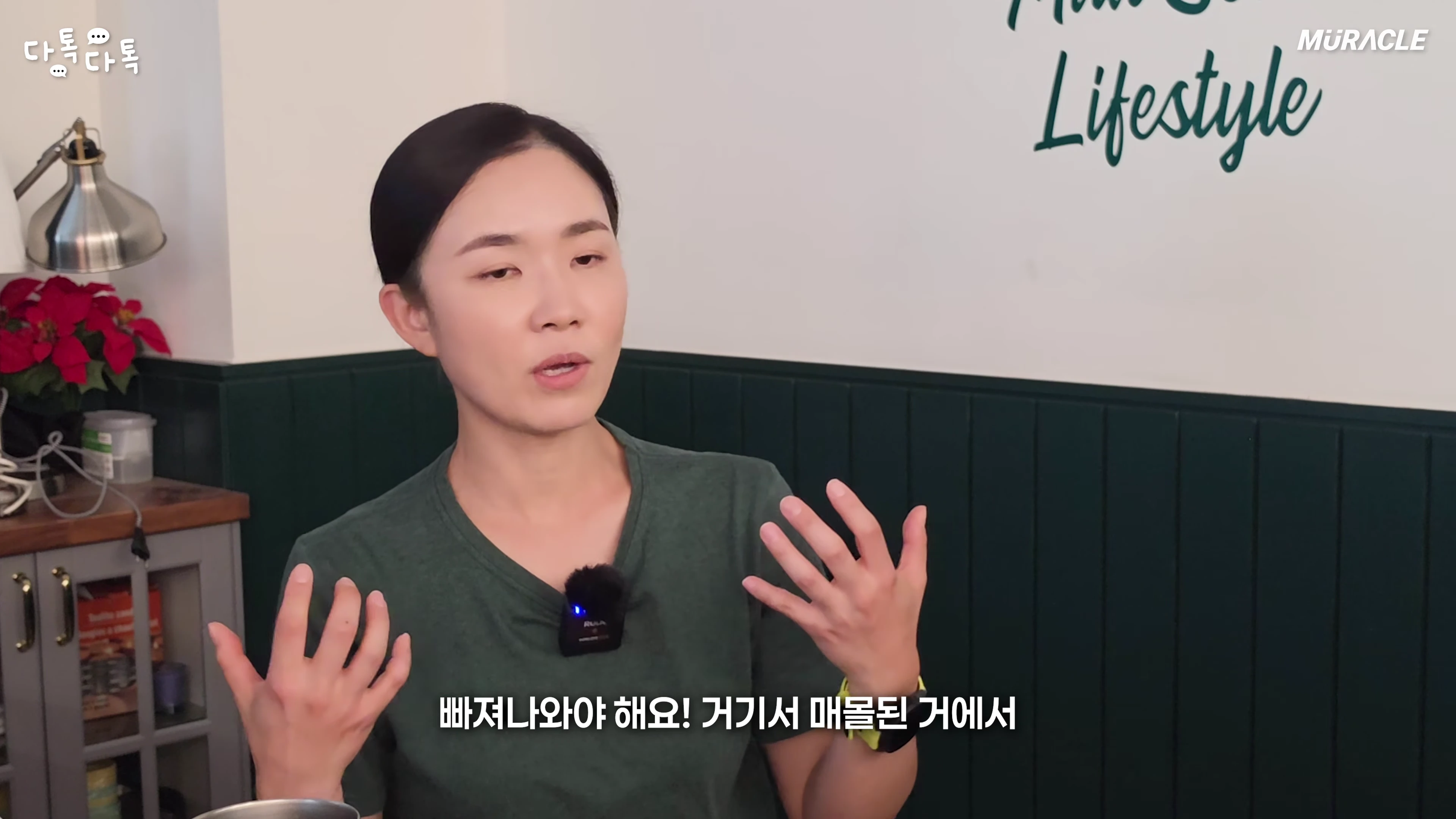 녹색 티셔츠를 입은 여성이 실내에서 손짓하며 이야기를 나누고 있는 모습