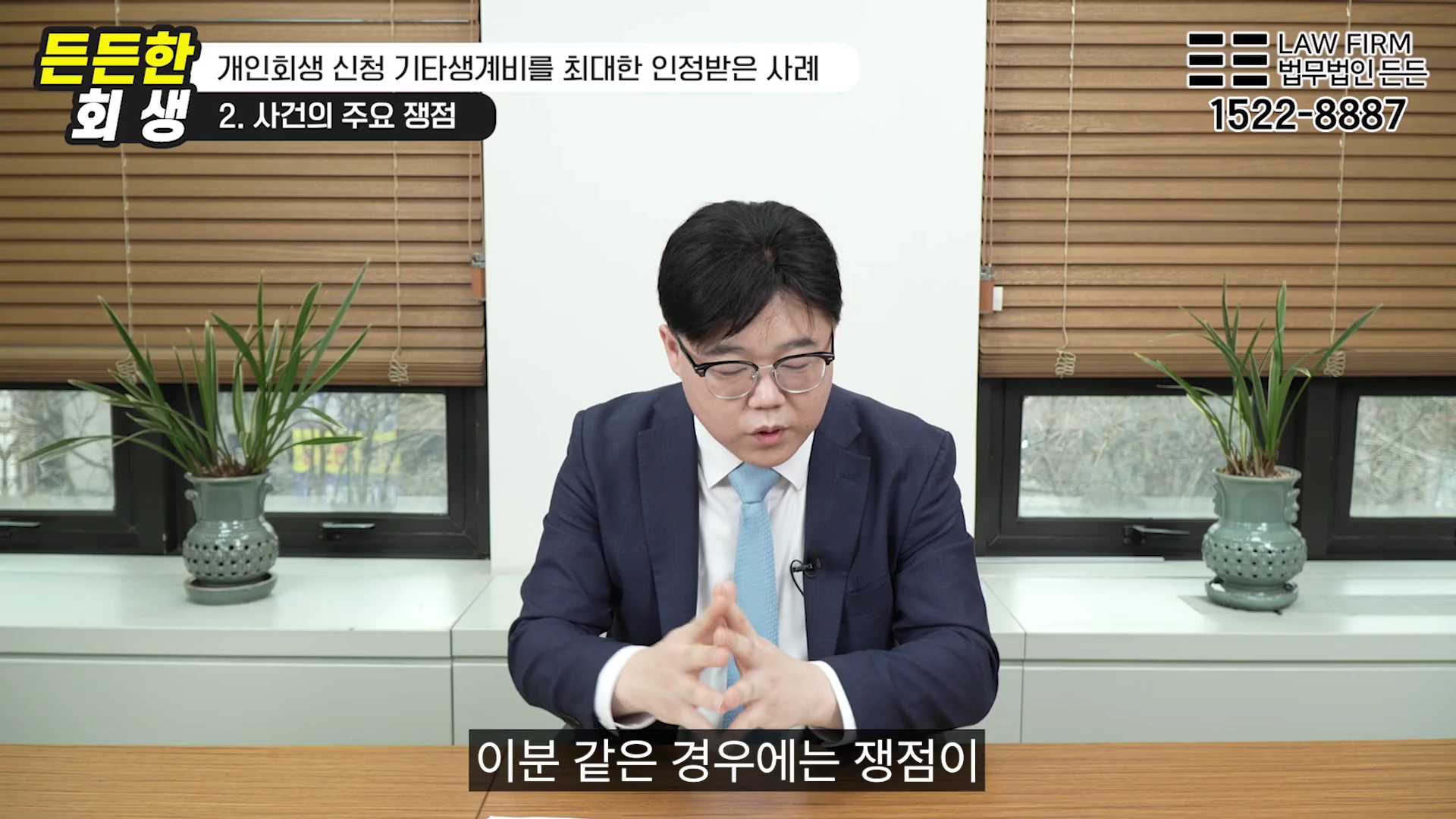 안경을 쓴 남성이 정장을 입고 책상 앞에 앉아 인터뷰를 진행하고 있으며, 화면 상단에는 '개인회생 신청 기타생계비를 최대한 인정받은 사례'라는 자막이 떠 있습니다.