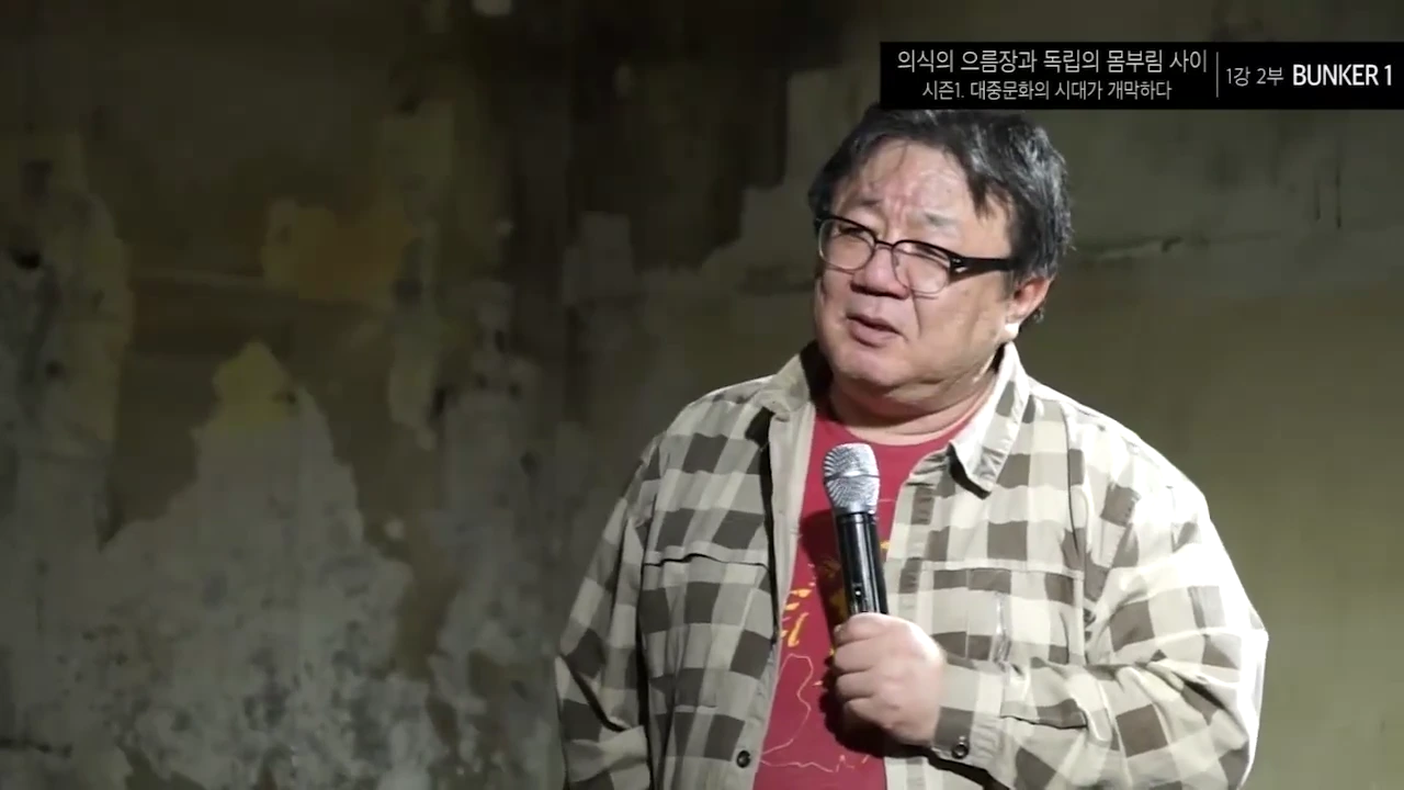 안경을 쓴 중년 남성이 마이크를 들고 강연하는 모습