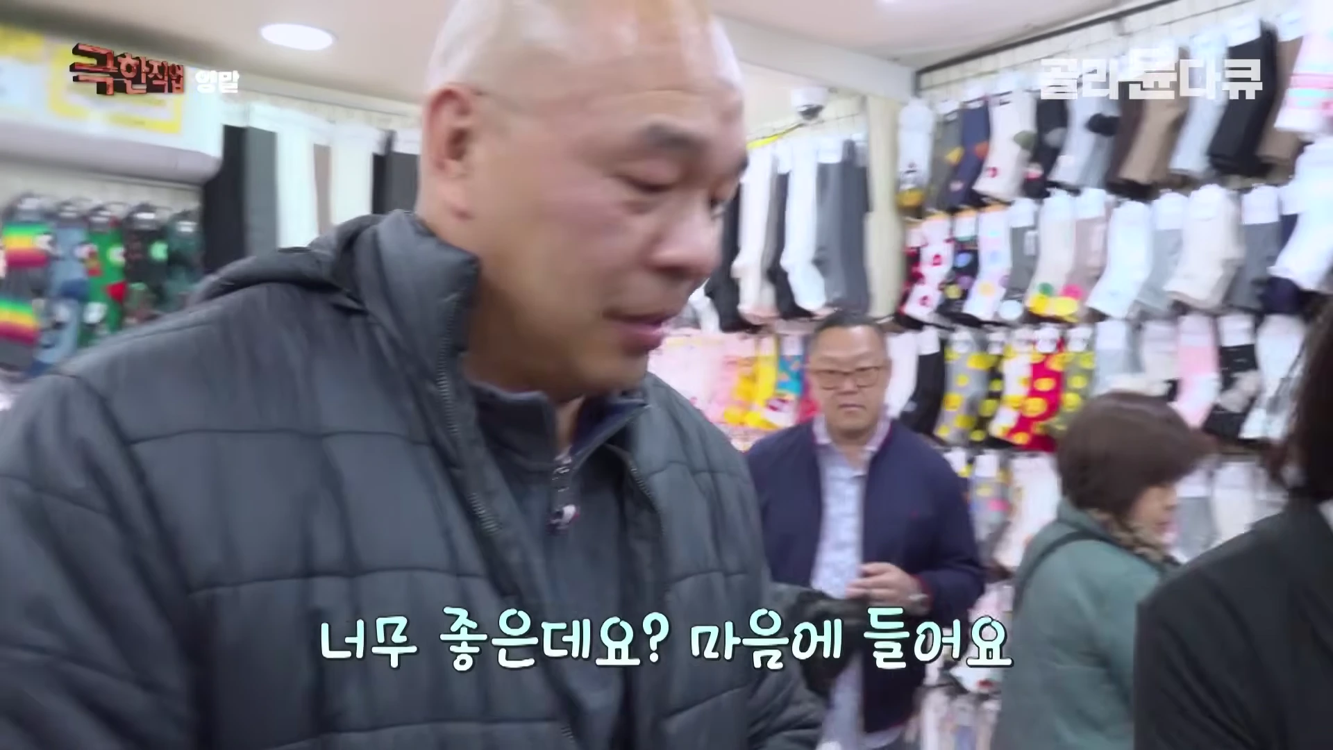 다양한 디자인의 양말이 벽면 가득 진열된 매장에서 한 남성이 인터뷰하고 있다.