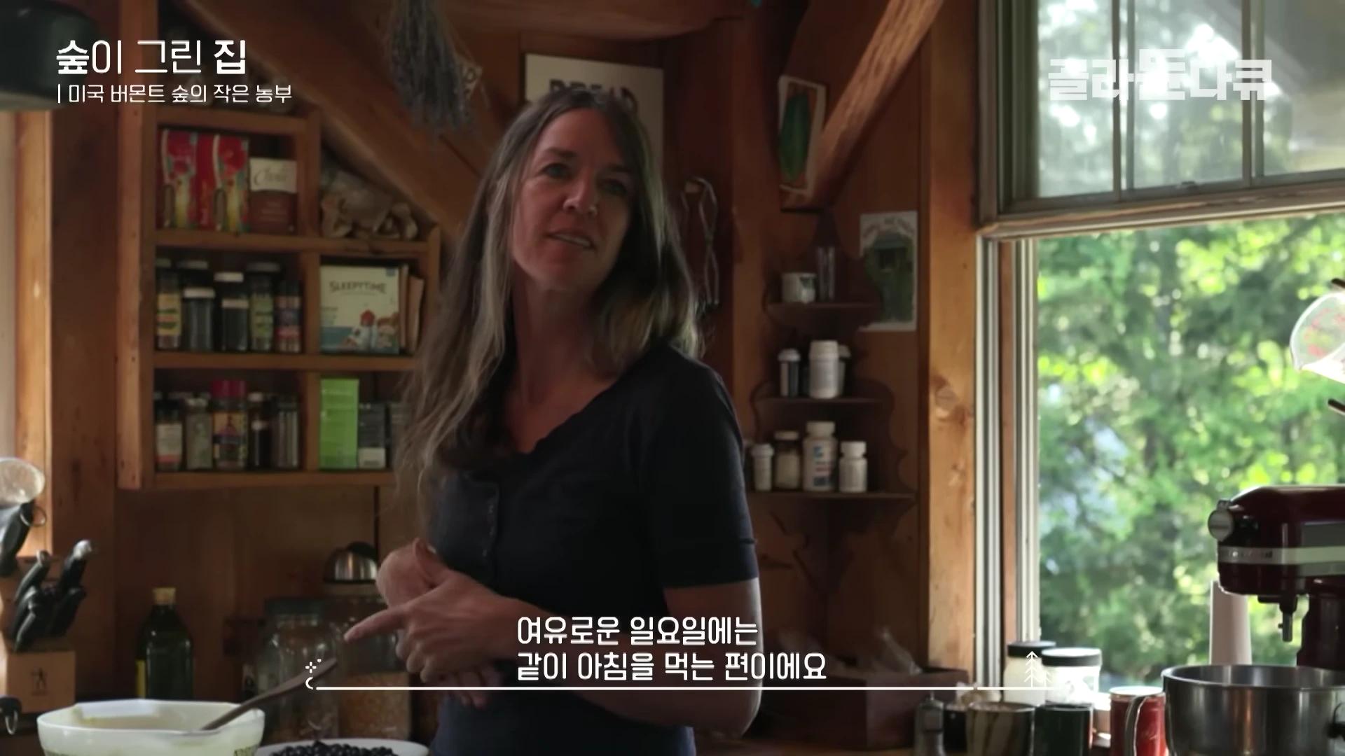 나무로 된 주방에서 긴 머리의 여성이 서서 이야기를 나누고 있는 모습