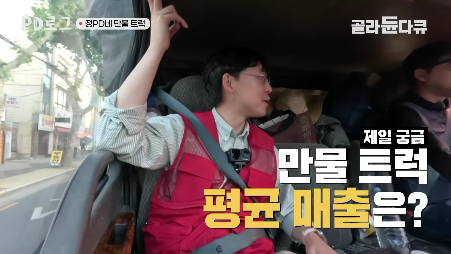 빨간 조끼를 입은 남성이 1톤 트럭 조수석에 앉아 운전석의 남성과 대화하는 모습