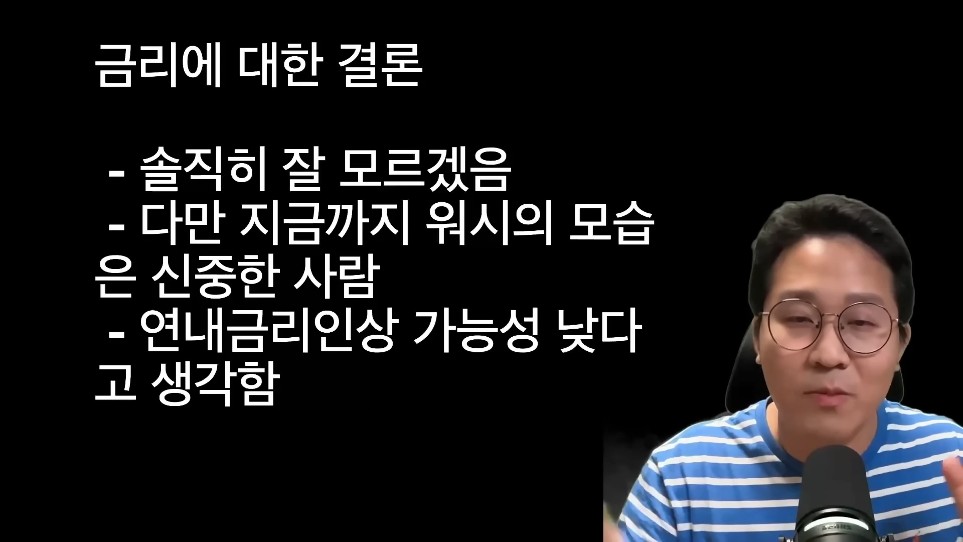 안경을 쓴 남성이 마이크 앞에서 금리에 대한 결론이 적힌 자막을 배경으로 이야기하고 있다.