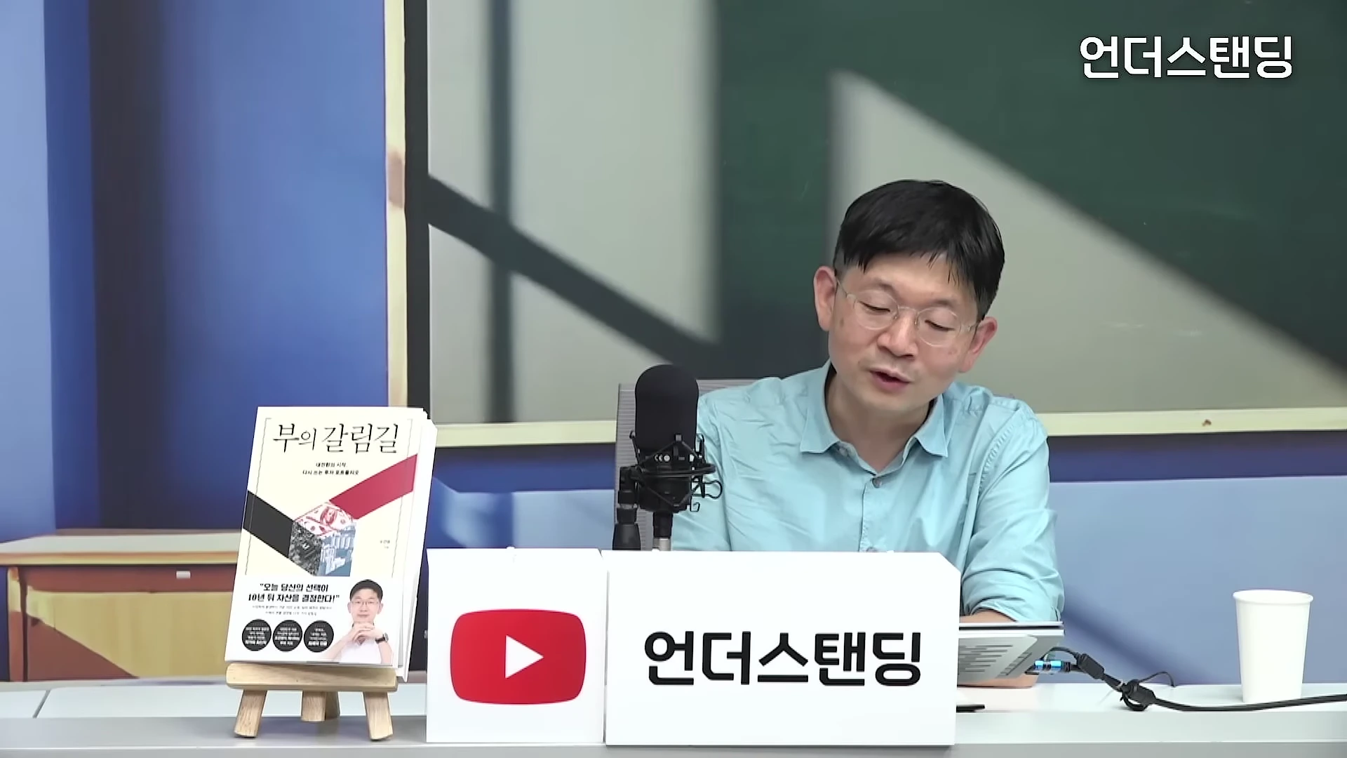 스튜디오에서 마이크 앞에 앉아 이야기를 나누는 안경 쓴 남성 출연자