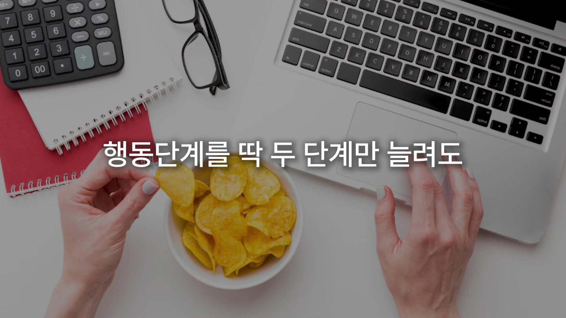 노트북과 계산기가 놓인 책상에서 한 사람이 감자칩을 집어 들고 있는 모습