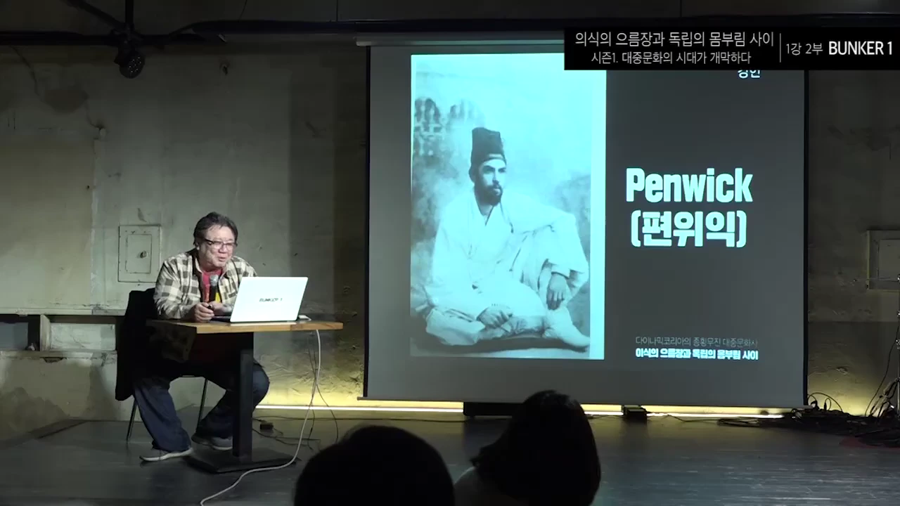 강연자가 노트북 앞에 앉아 있고, 뒤편 스크린에는 한복을 입은 외국인 편위익의 흑백 사진이 투사되어 있다.