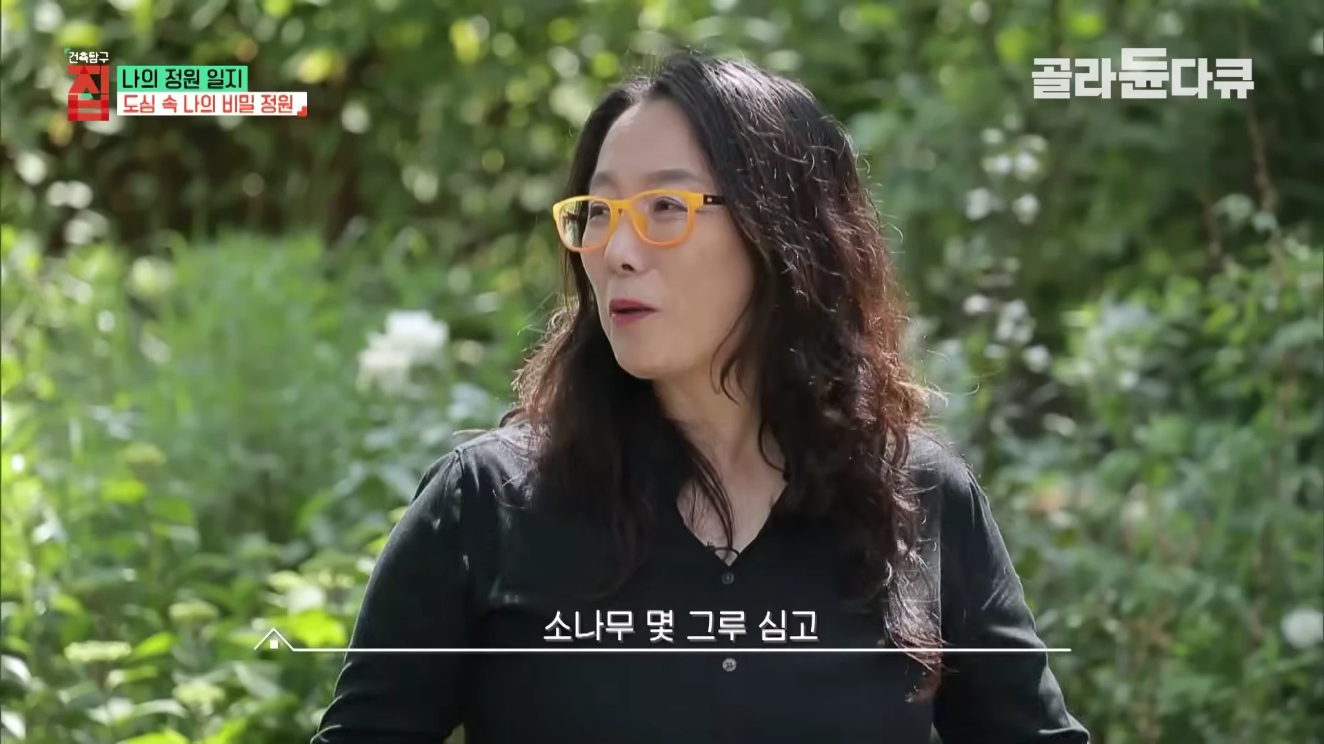 주황색 안경을 쓴 여성이 푸른 정원을 배경으로 인터뷰하고 있는 모습