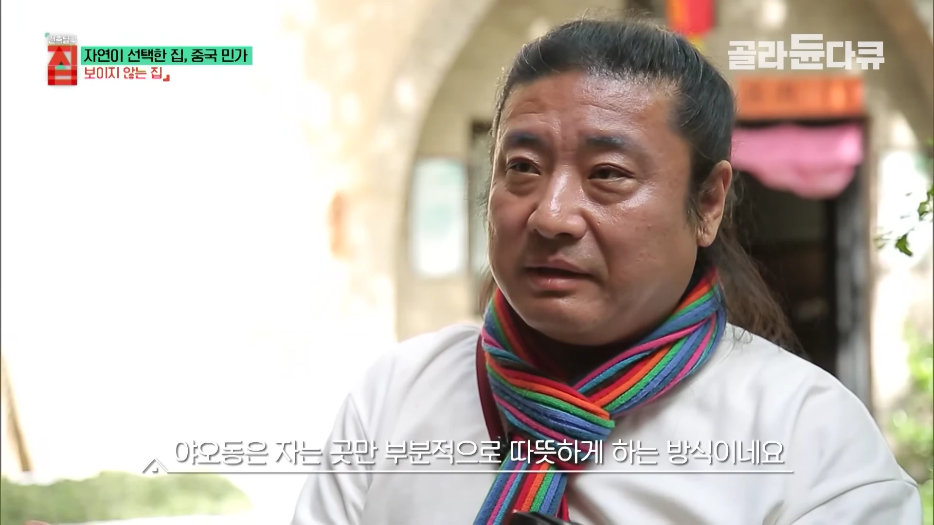 화려한 무지개색 스카프를 두른 남성이 인터뷰하는 모습