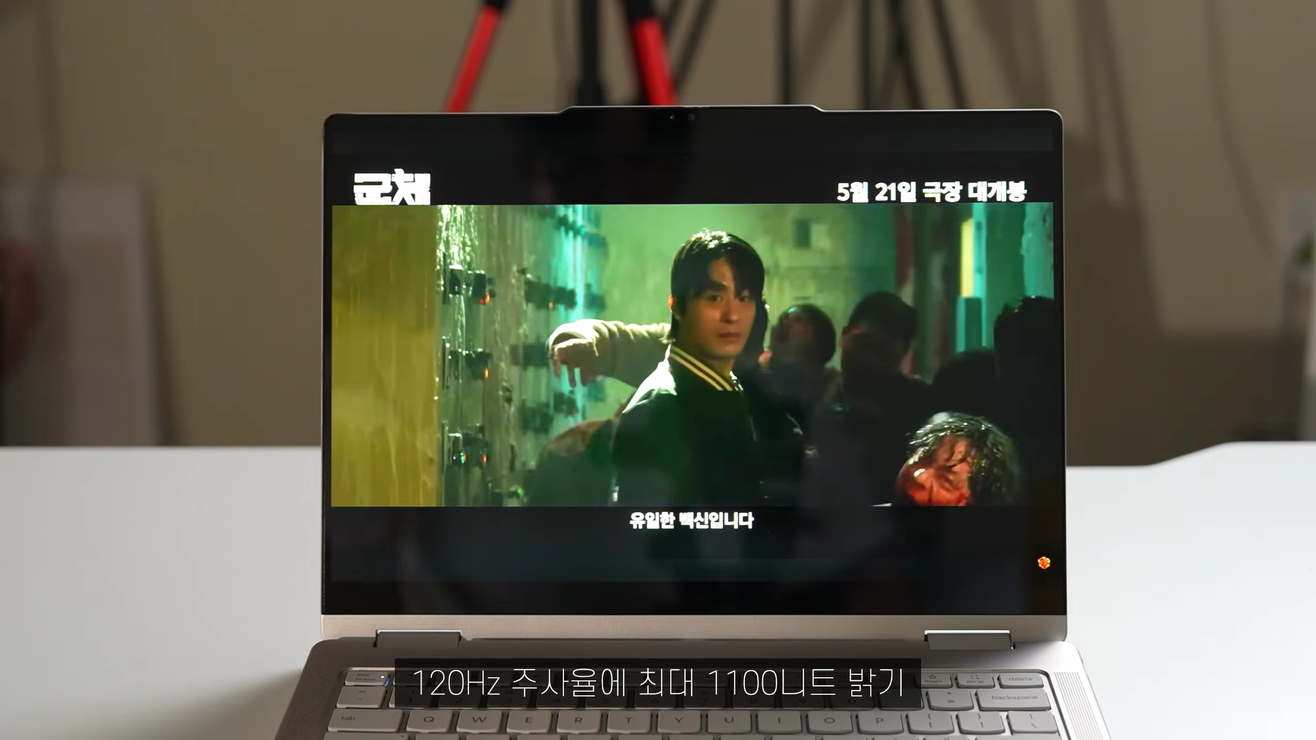 노트북 화면에 영화 예고편이 재생되고 있으며, 하단에는 120Hz 주사율과 1100니트 밝기라는 텍스트가 표시되어 있습니다.