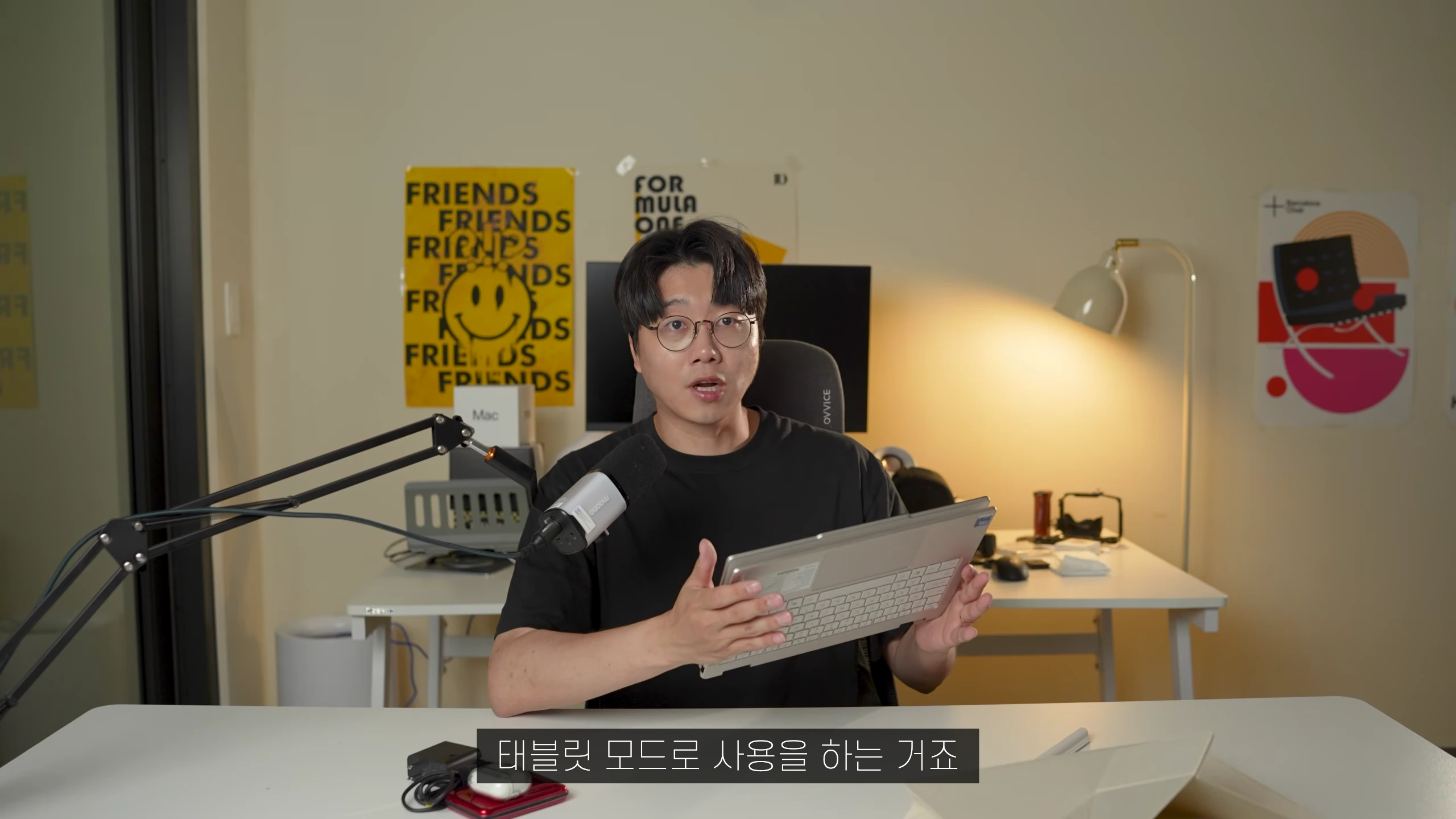 안경을 쓴 남성이 책상에 앉아 노트북을 태블릿 모드로 접어 보여주고 있는 모습