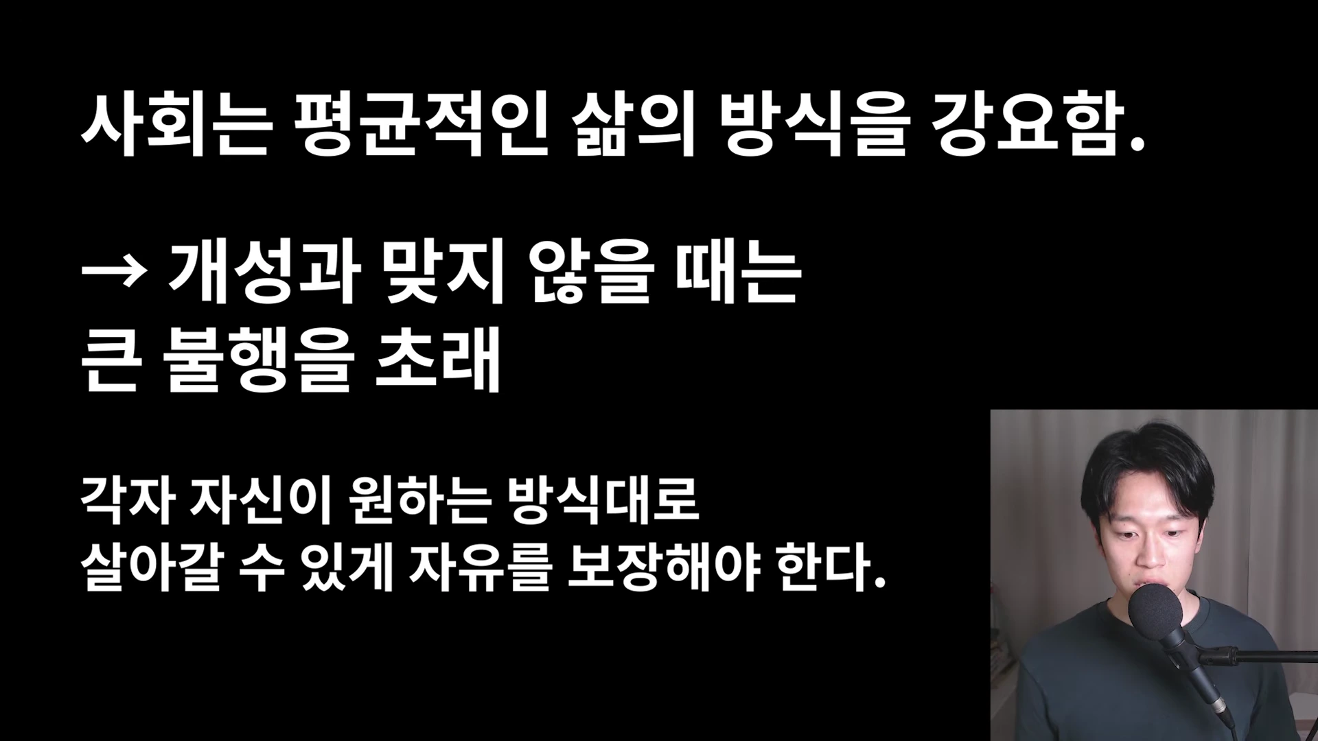 검은 배경에 흰색 글자로 사회의 획일적 강요와 개인의 자유를 강조하는 문구가 적힌 화면과 마이크 앞에 앉은 남성.