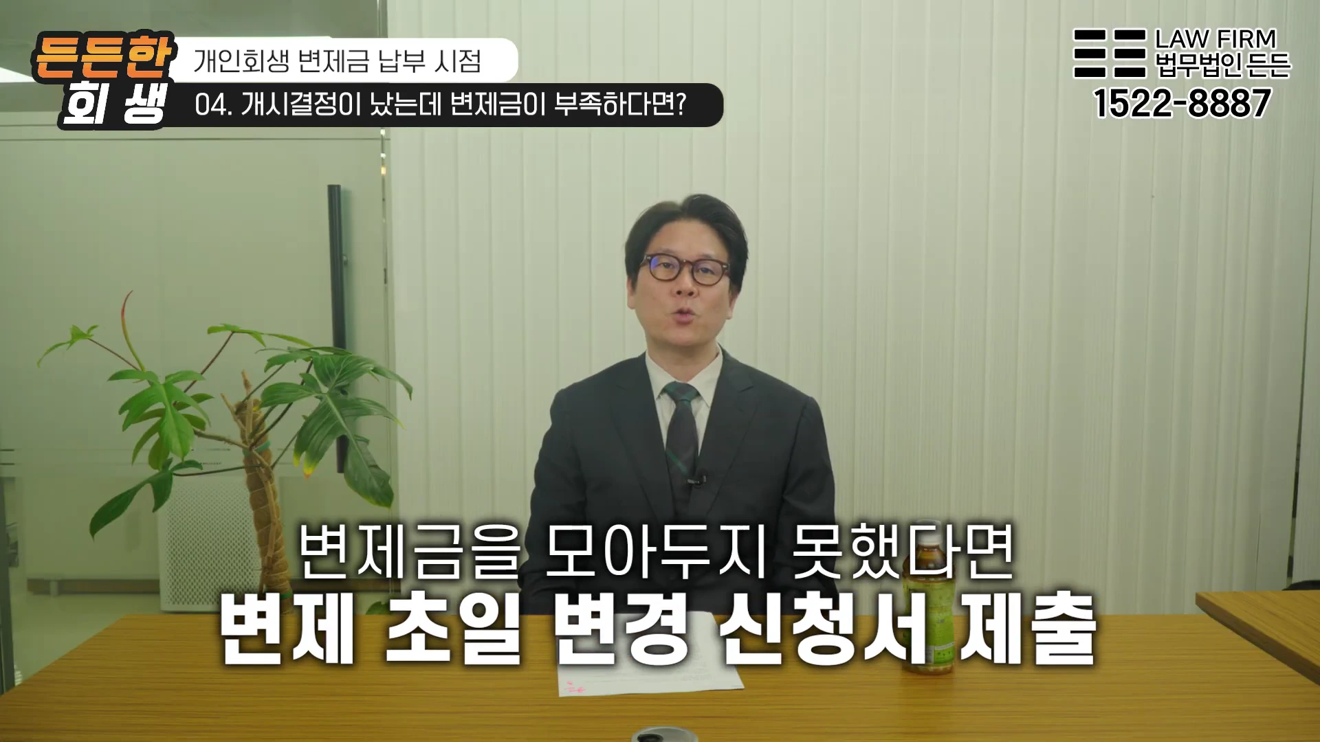 정장을 입은 남성이 사무실 책상에 앉아 카메라를 보며 설명하는 모습