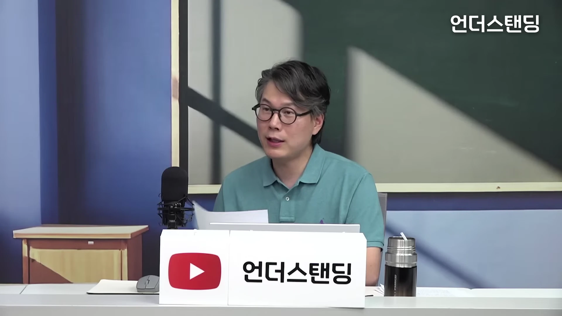 안경을 쓴 남성이 스튜디오 책상 앞에 앉아 마이크를 앞에 두고 이야기를 나누고 있다.