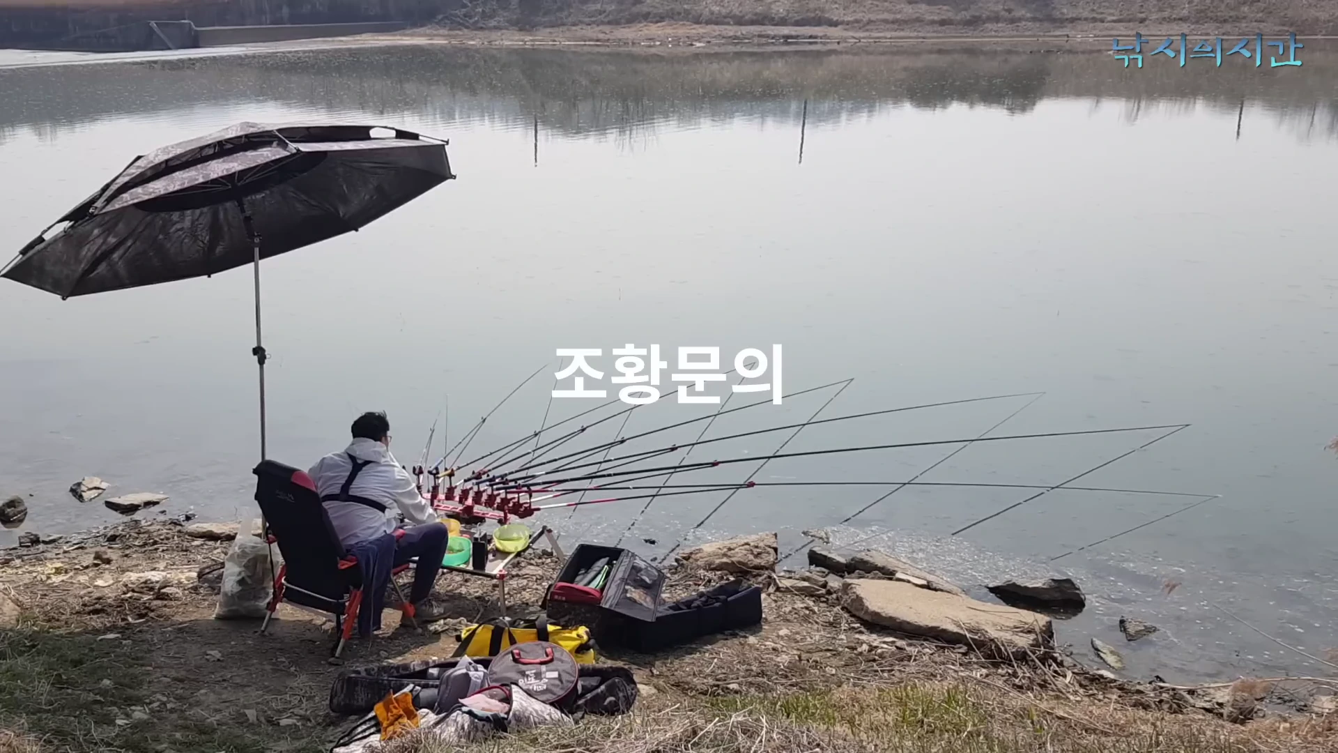 강가에 앉아 여러 대의 낚싯대를 펼쳐놓고 낚시를 즐기는 낚시꾼의 뒷모습