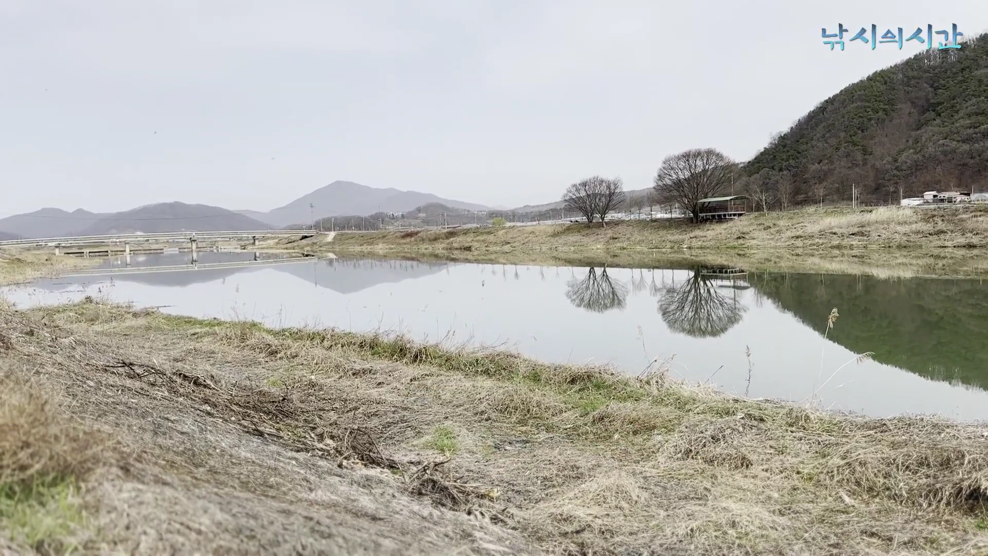 잔잔한 강물과 멀리 산이 보이는 평화로운 낚시터 전경