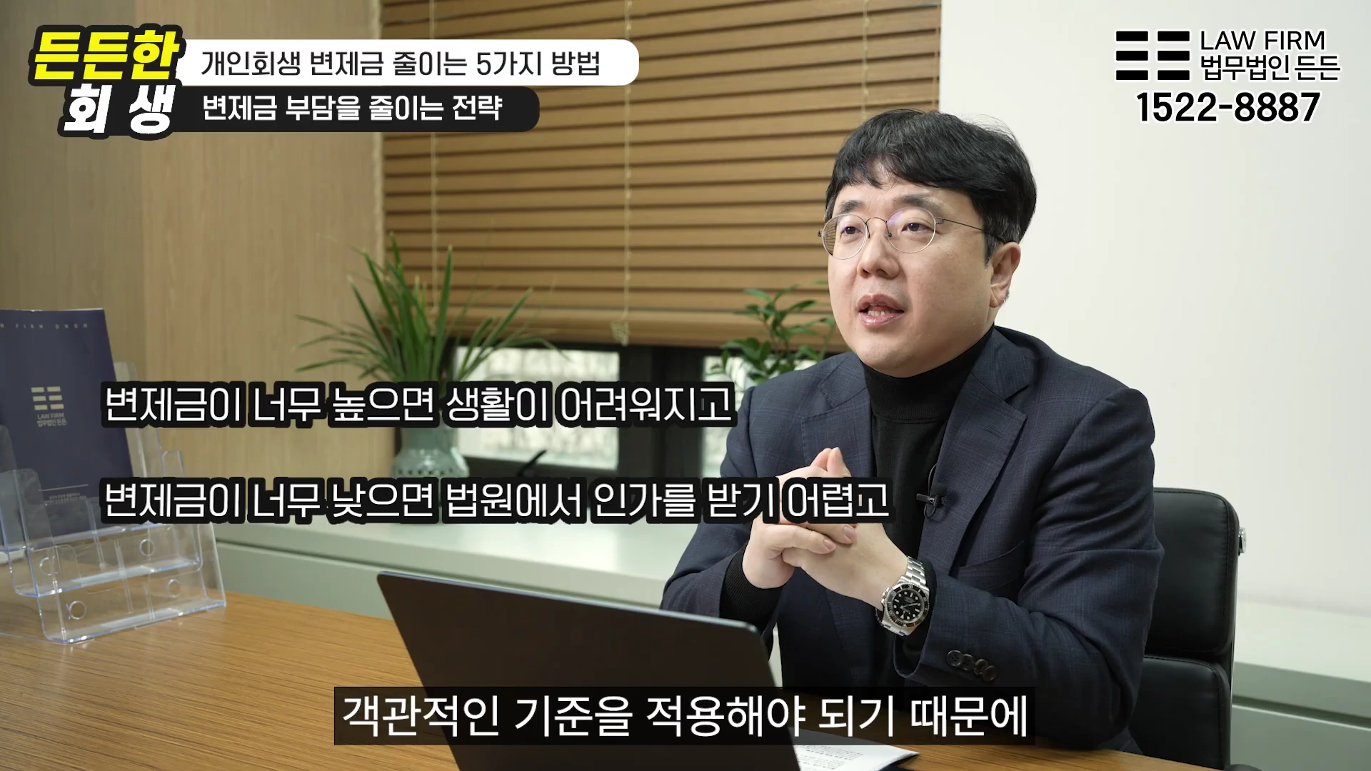 안경을 쓴 남성 변호사가 사무실 책상에 앉아 개인회생 변제금에 대해 설명하고 있는 모습