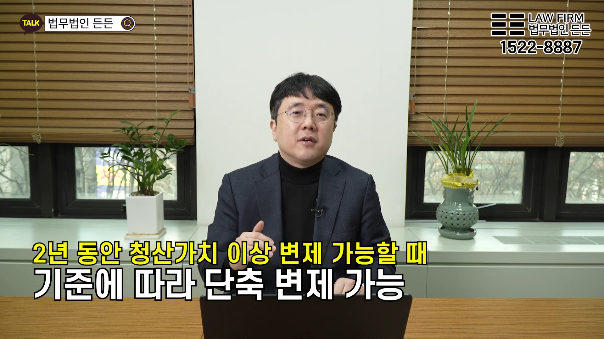 안경을 쓴 남성이 사무실 책상에 앉아 카메라를 보며 설명하고 있고, 화면 하단에는 변제 기간 단축에 관한 자막이 적혀 있습니다.