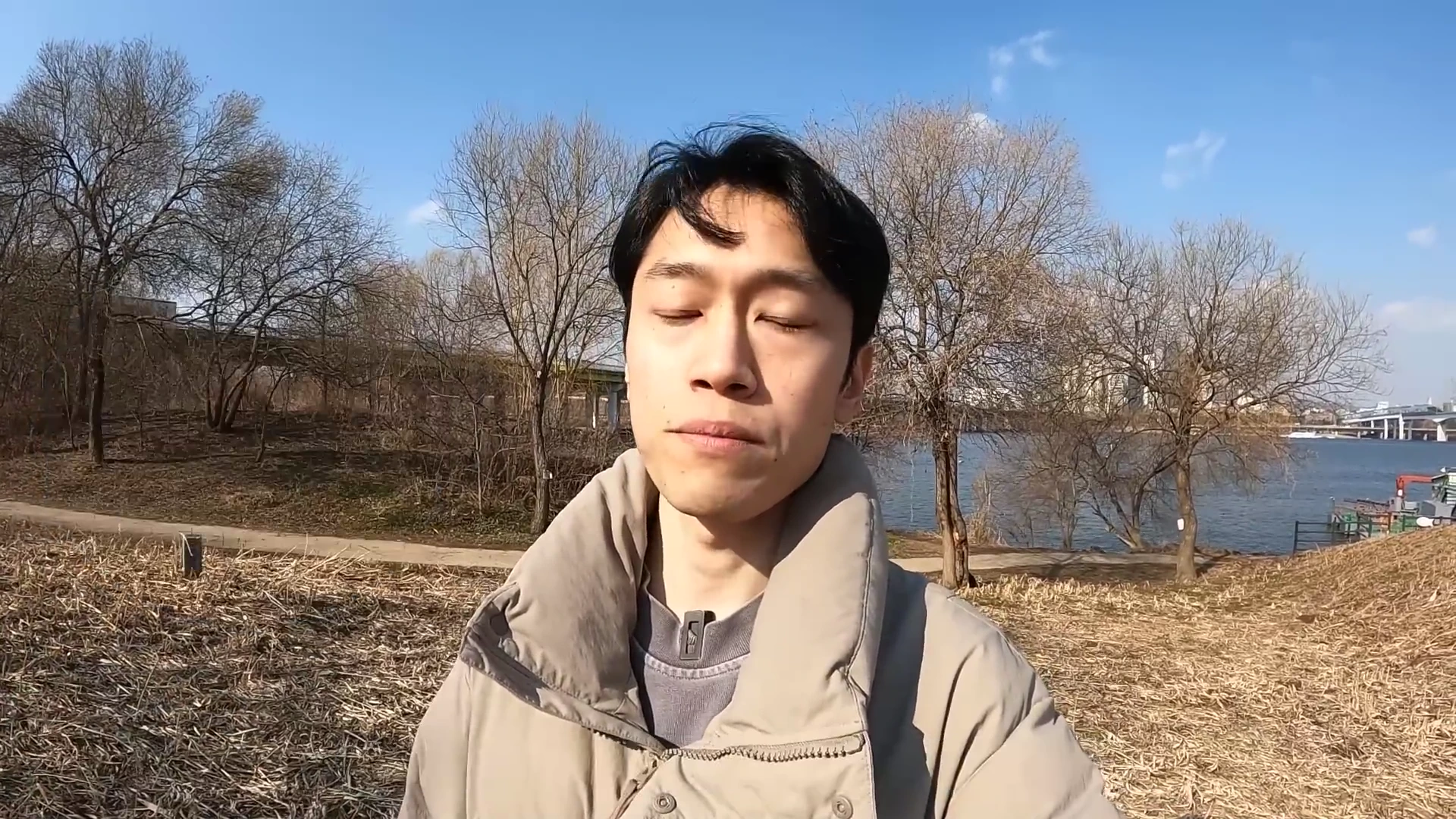 야외 강변을 배경으로 눈을 감고 서 있는 한 남성