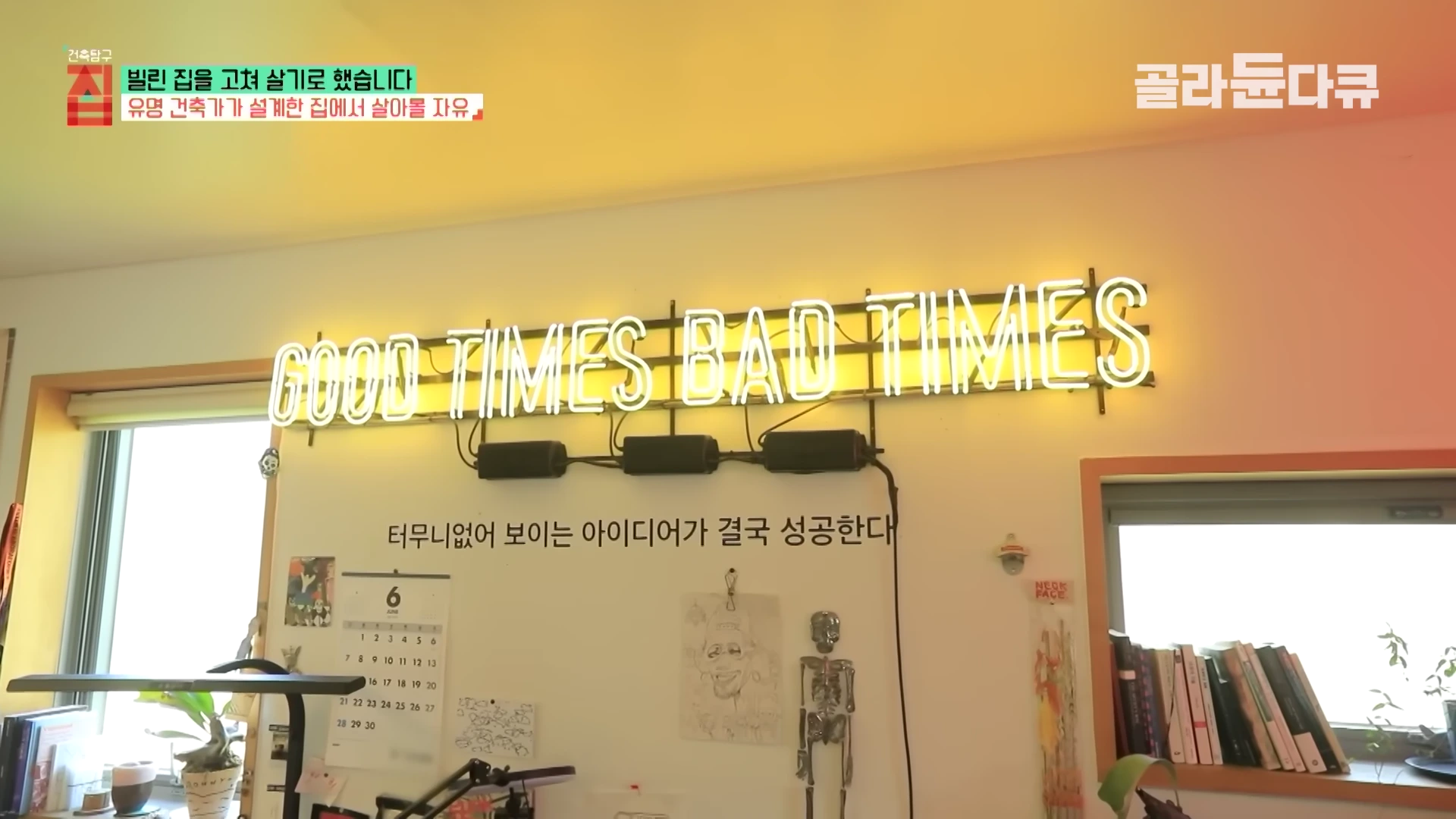 벽면에 'GOOD TIMES BAD TIMES'라는 노란색 네온사인 문구와 함께 달력, 그림, 해골 모형 등이 장식된 실내 벽면