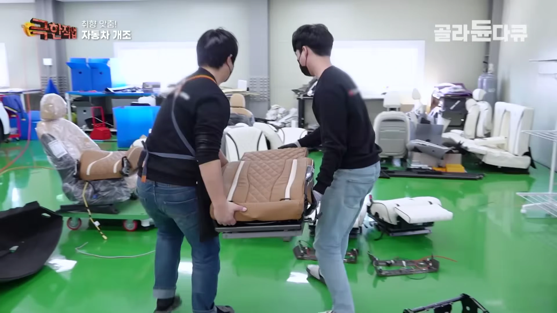 작업장에서 두 명의 작업자가 완성된 자동차 가죽 시트를 조심스럽게 옮기고 있다.