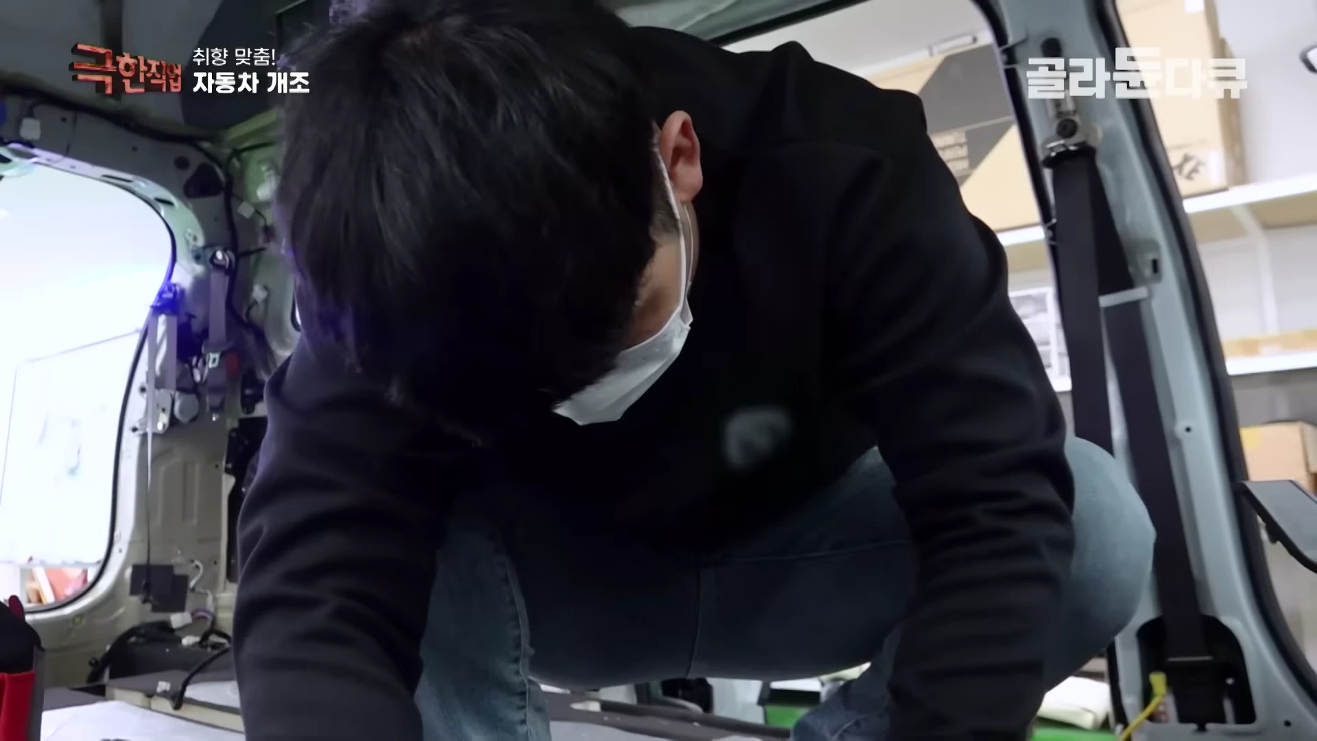 자동차 개조 공장에서 작업자가 차량 내부 바닥 매트를 걷어내고 배선 작업을 준비하고 있다.