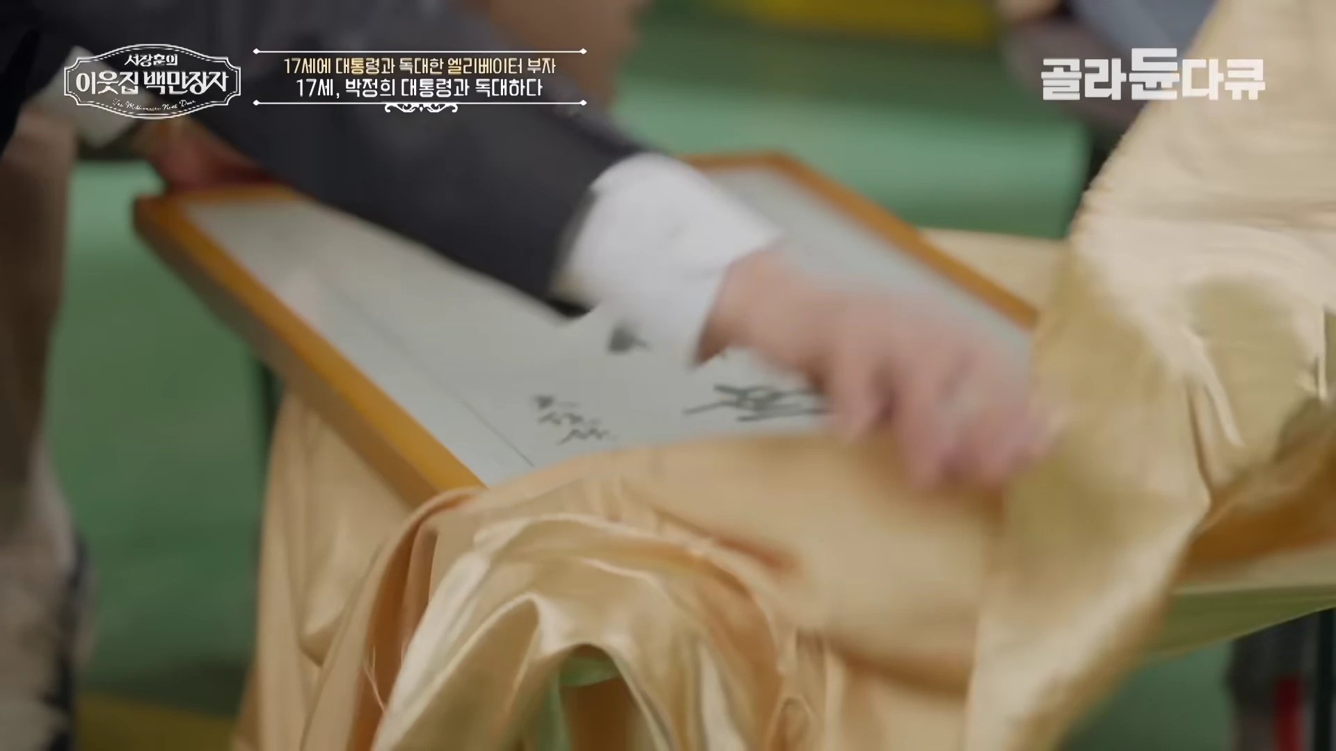 한 남성이 금색 천으로 덮인 액자를 조심스럽게 벗겨내고 있는 모습