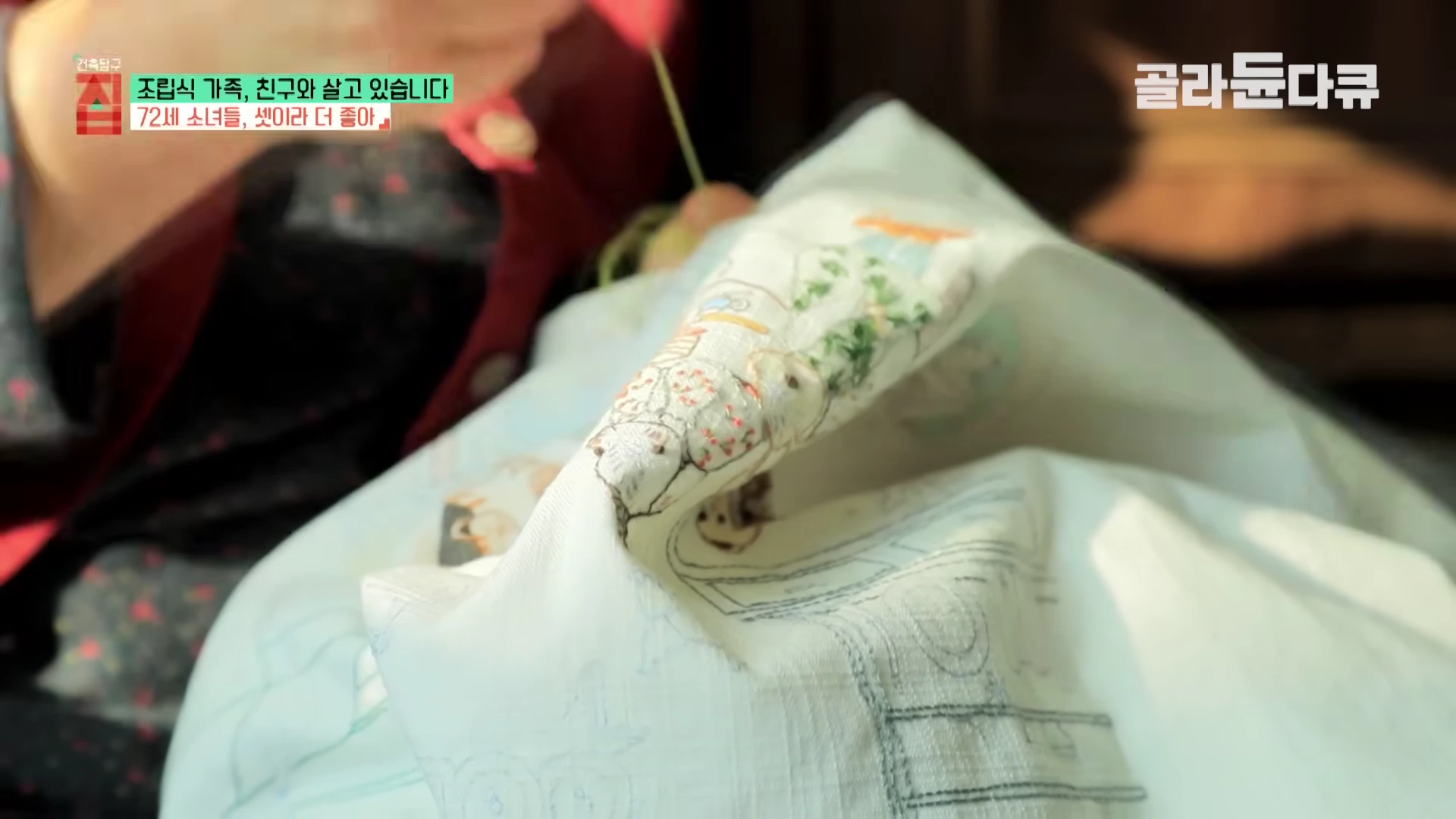 한 노인이 밝은 천 위에 섬세하게 자수를 놓고 있는 모습