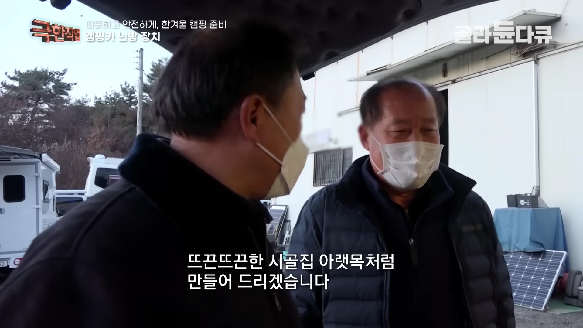 마스크를 쓴 두 남성이 캠핑카 앞에서 대화를 나누고 있는 모습