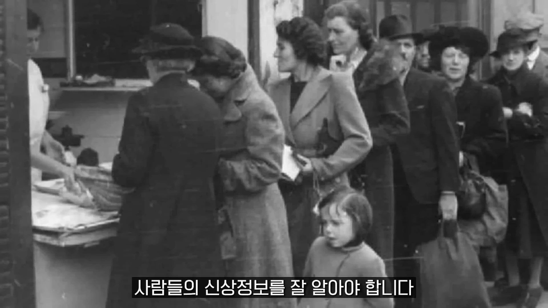흑백 사진 속에서 코트를 입은 사람들이 배급을 받기 위해 길게 줄을 서 있는 모습