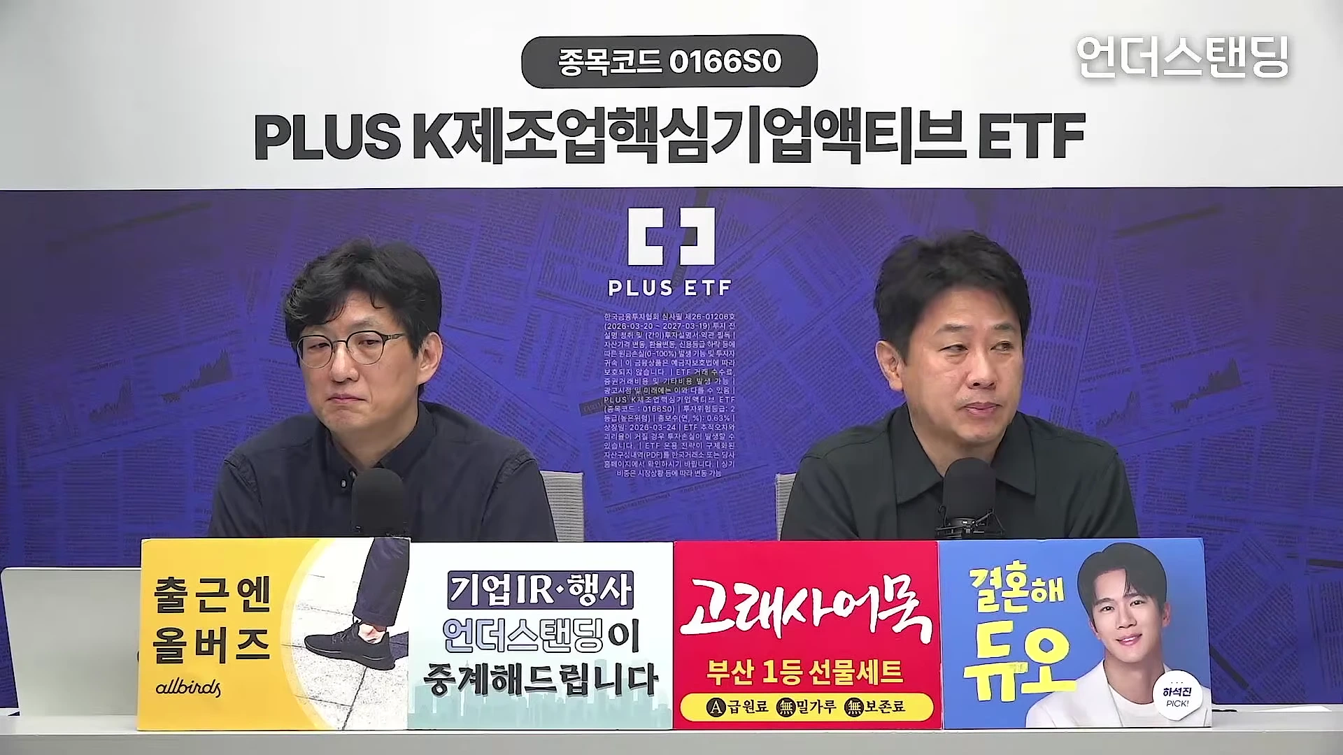스튜디오에서 두 남성이 마이크 앞에 앉아 대화를 나누고 있으며, 앞쪽에는 다양한 광고 문구가 적힌 패널들이 놓여 있습니다.