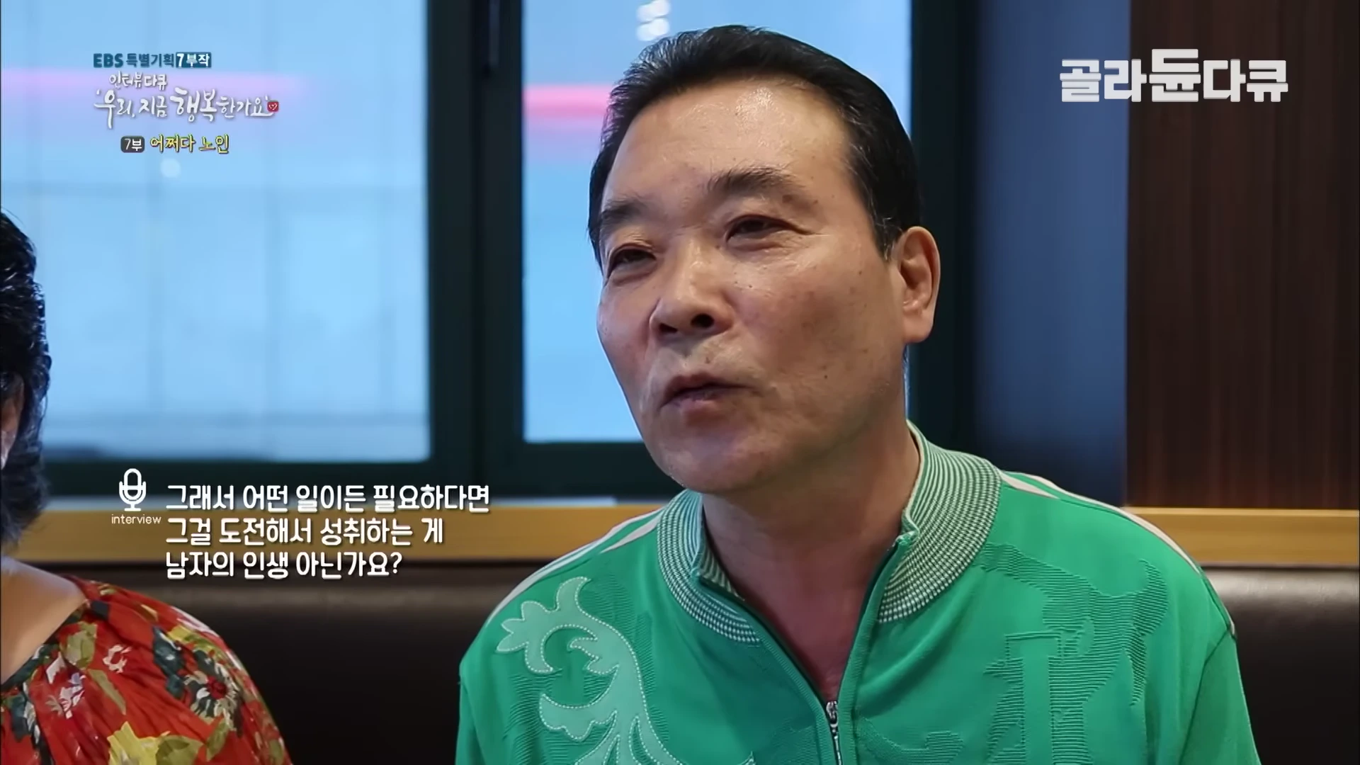 초록색 트레이닝복을 입은 중년 남성이 인터뷰하며 진지하게 이야기하고 있다.