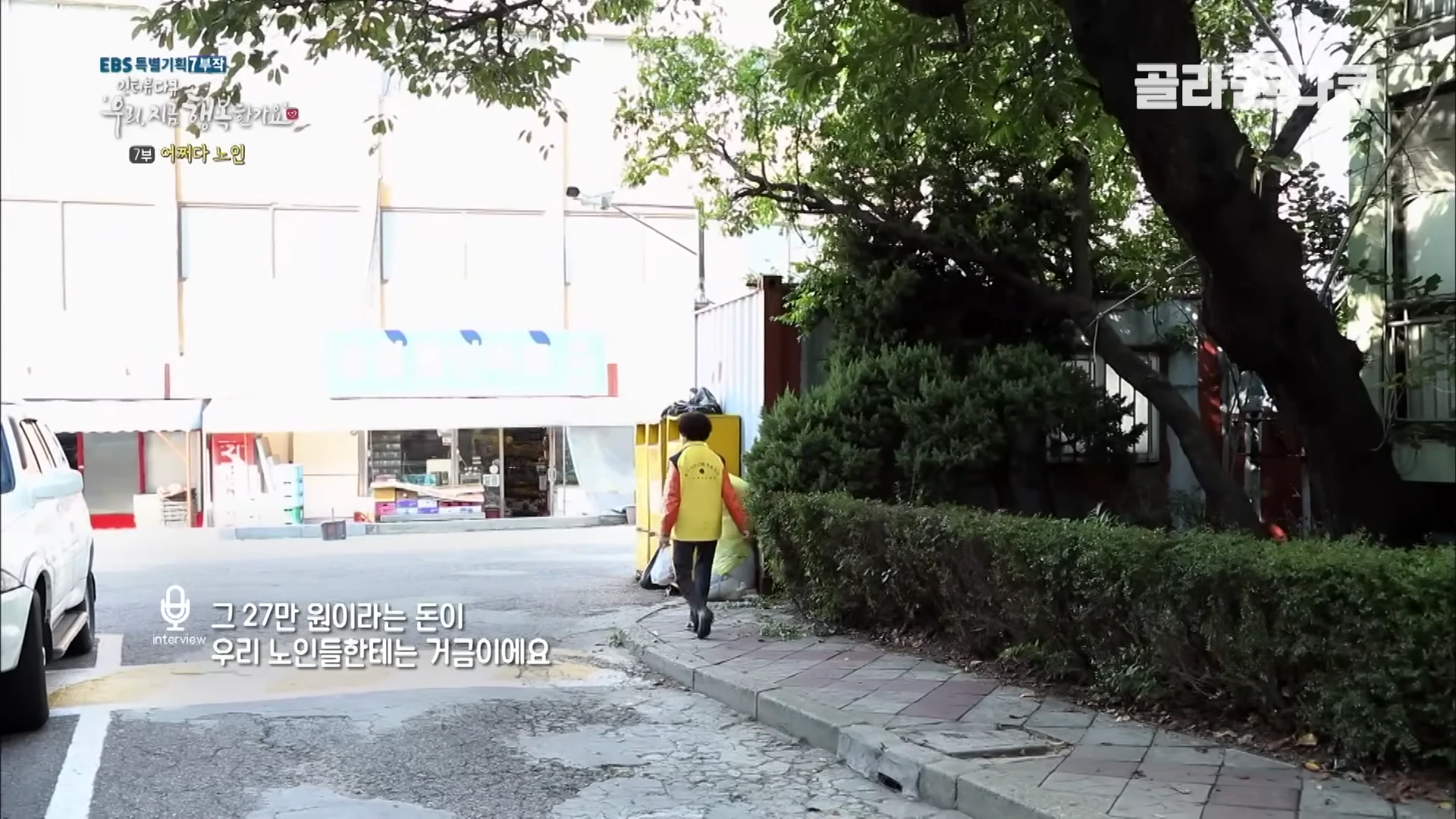 노란색 조끼를 입은 노인이 골목길을 걸어가고 있는 모습