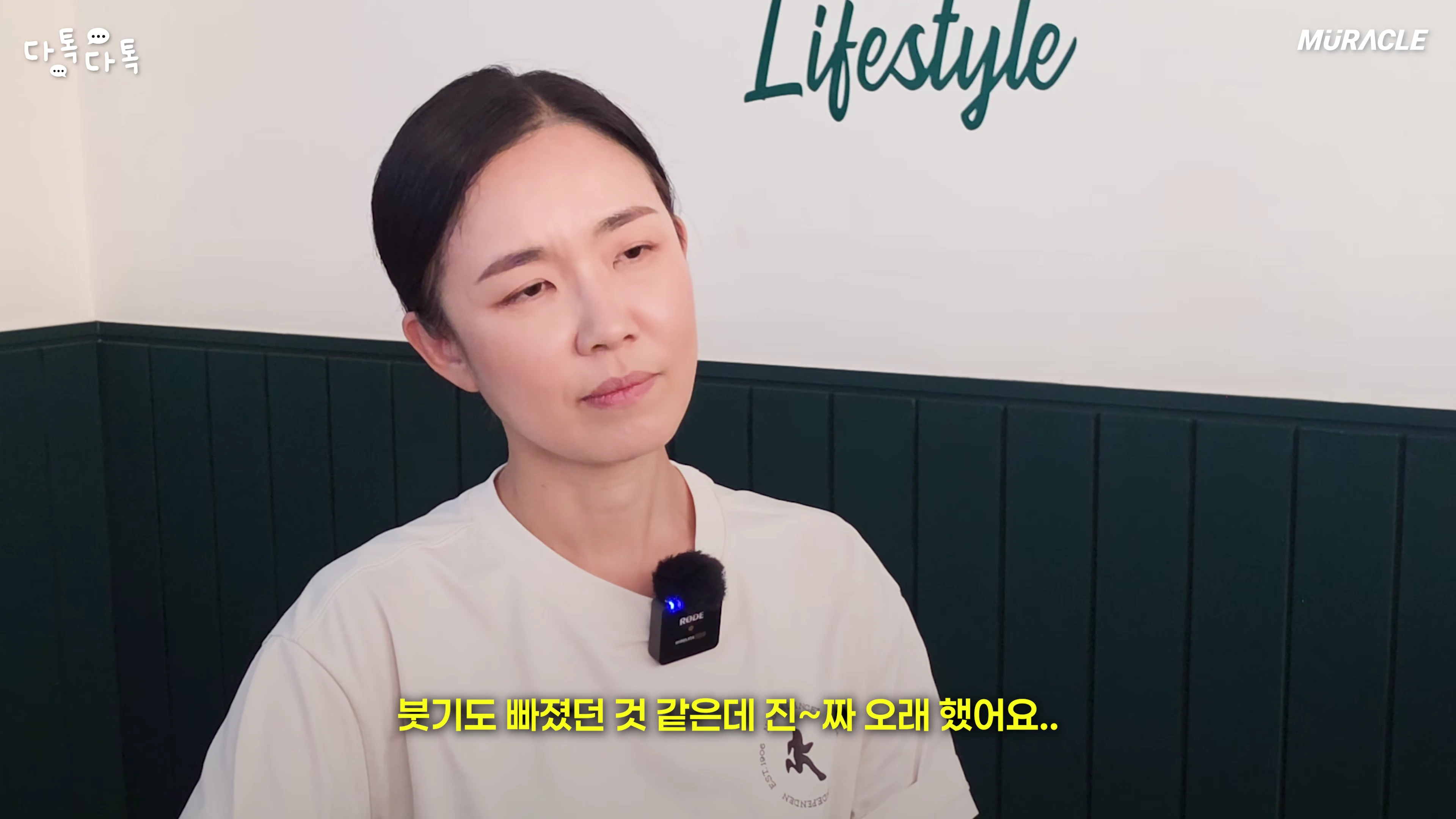흰색 티셔츠를 입은 여성이 실내에서 인터뷰를 진행하고 있으며, 화면 하단에는 자막이 표시되어 있습니다.