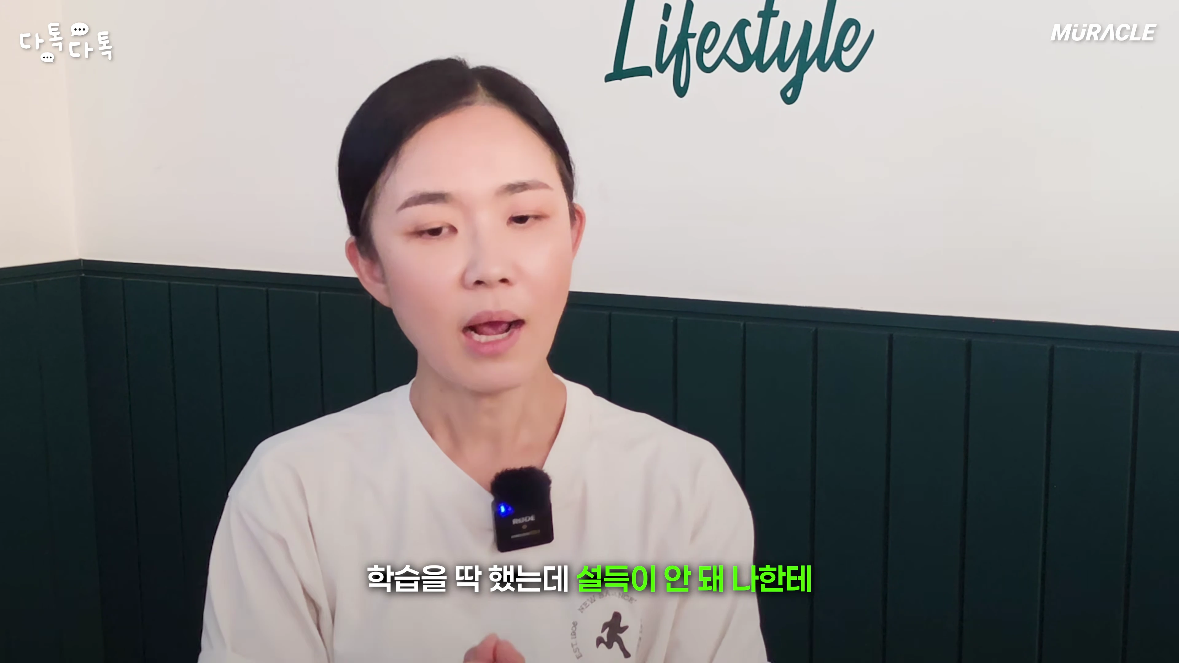 흰색 티셔츠를 입은 여성이 실내에서 카메라를 보며 이야기를 나누고 있는 모습