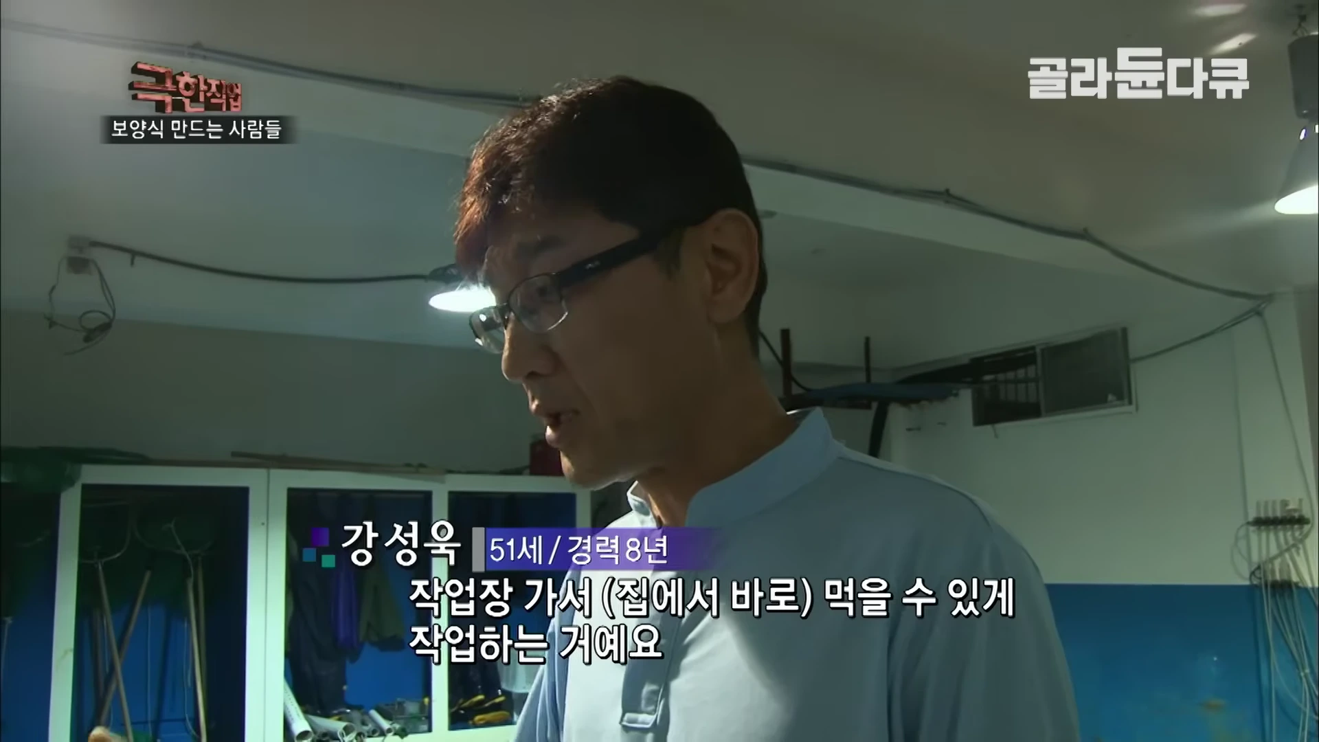 안경을 쓴 중년 남성이 실내 작업장에서 인터뷰하는 모습