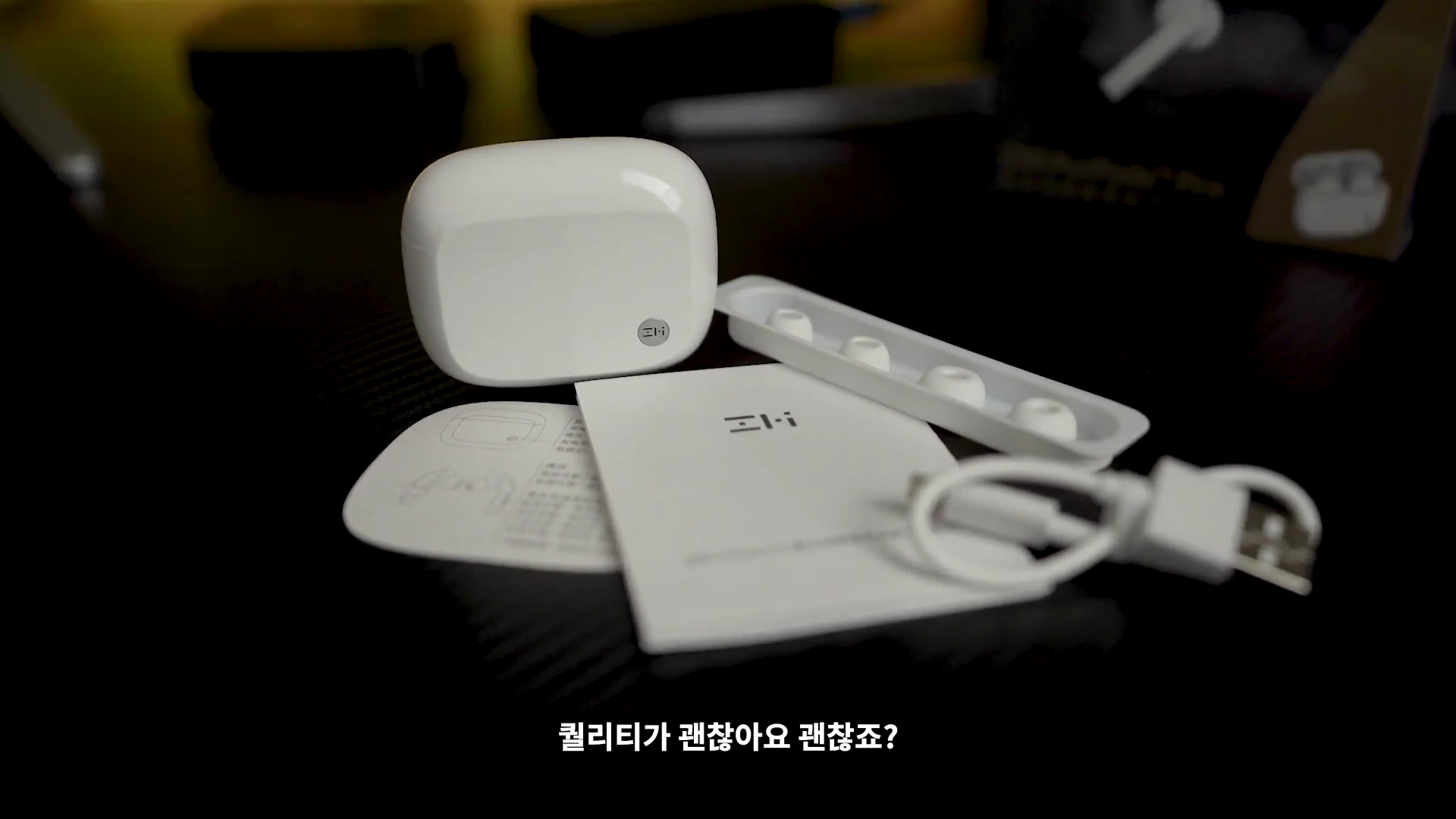 흰색 무선 이어폰 충전 케이스와 이어팁, 설명서, 충전 케이블이 검은색 테이블 위에 놓여 있다.