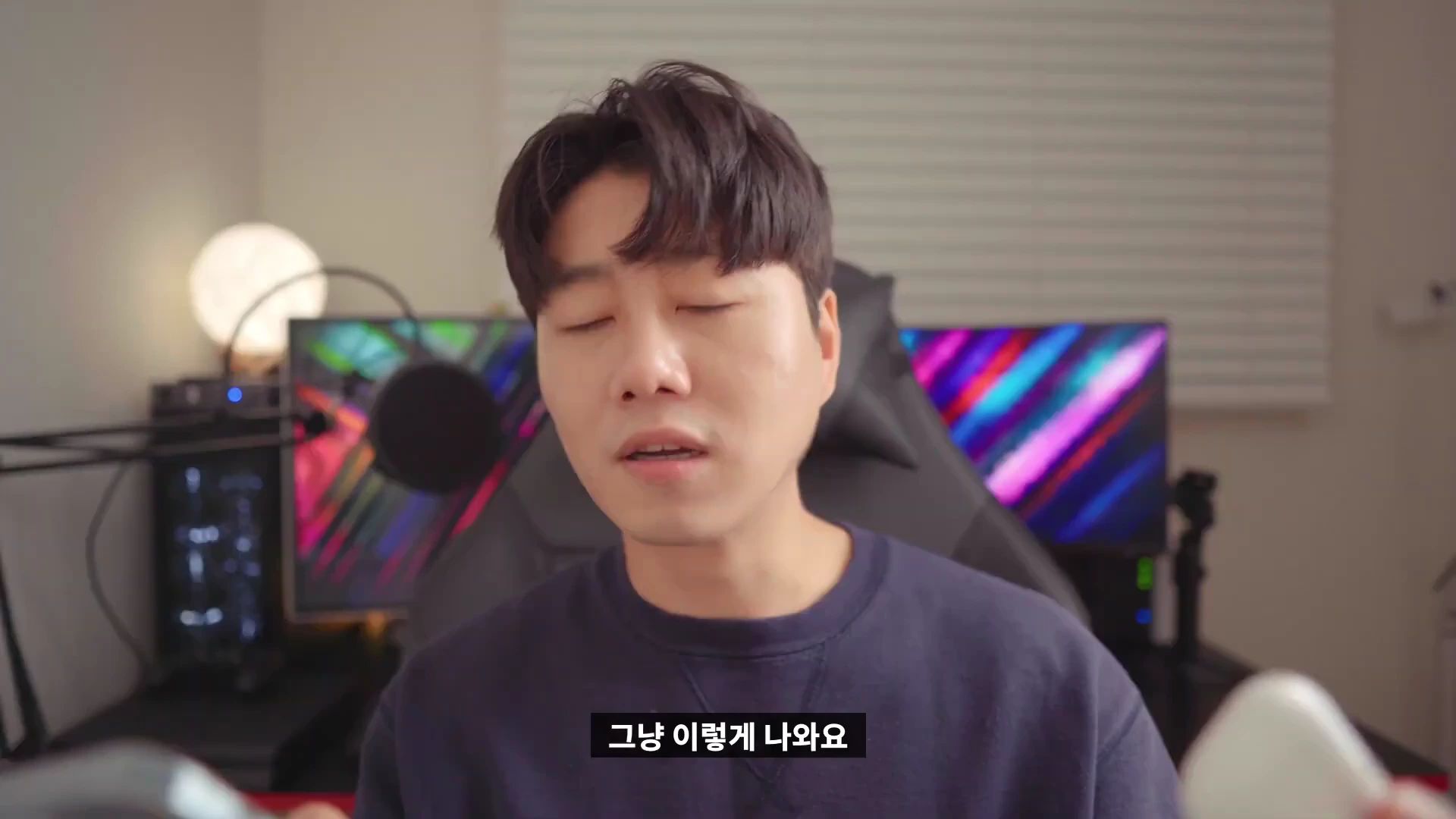 실내에서 검은색 상의를 입은 남성이 정면을 바라보며 무언가를 설명하고 있는 모습