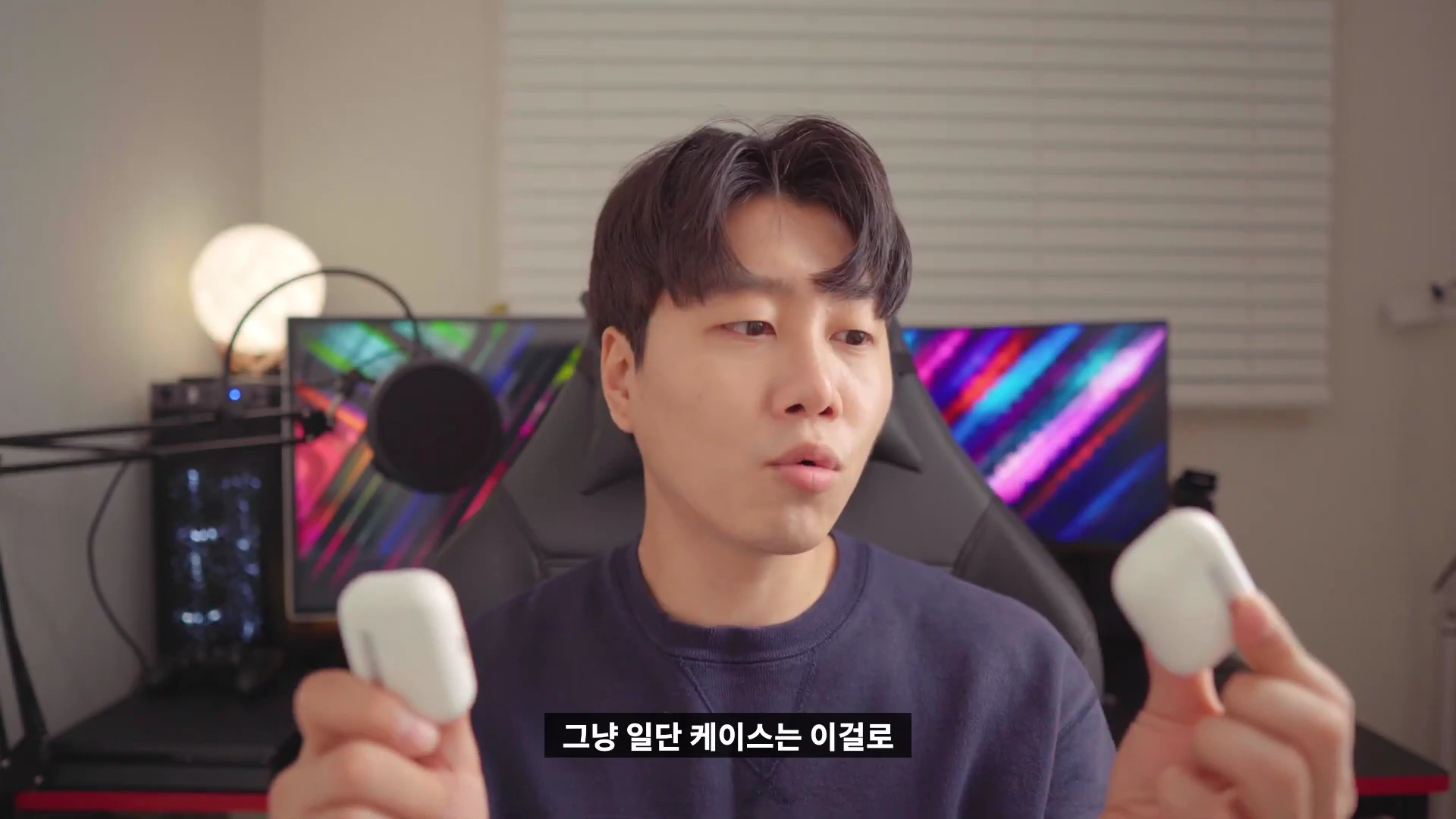 스튜디오에서 한 남성이 양손에 에어팟 프로 케이스를 하나씩 들고 비교하며 설명하고 있다.