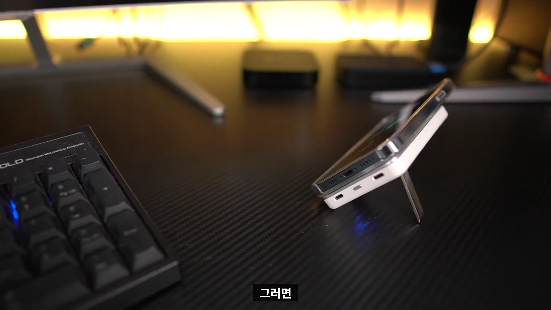 책상 위에 거치대 기능을 사용하여 비스듬히 세워진 스마트폰과 보조배터리