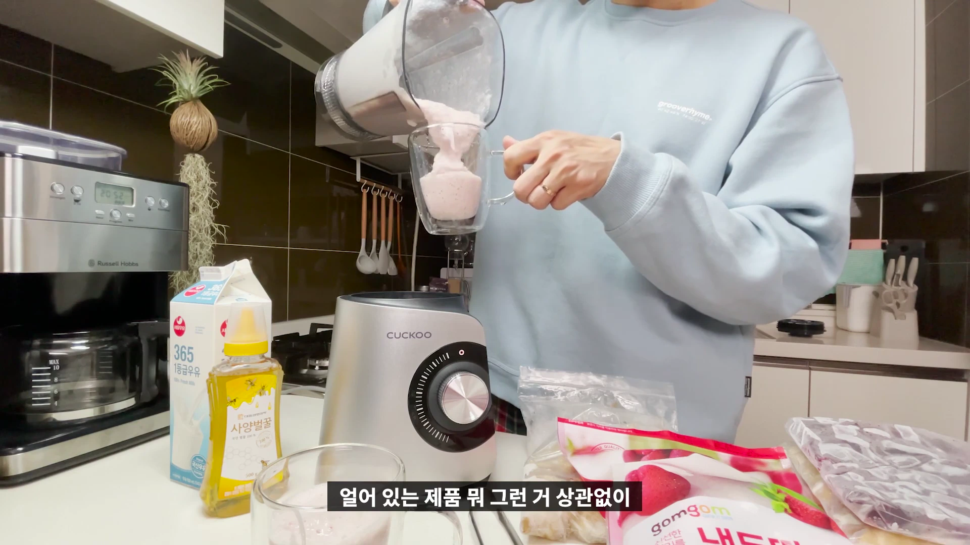 주방에서 한 사람이 믹서기 용기에 담긴 딸기 바나나 주스를 유리컵에 따르고 있는 모습
