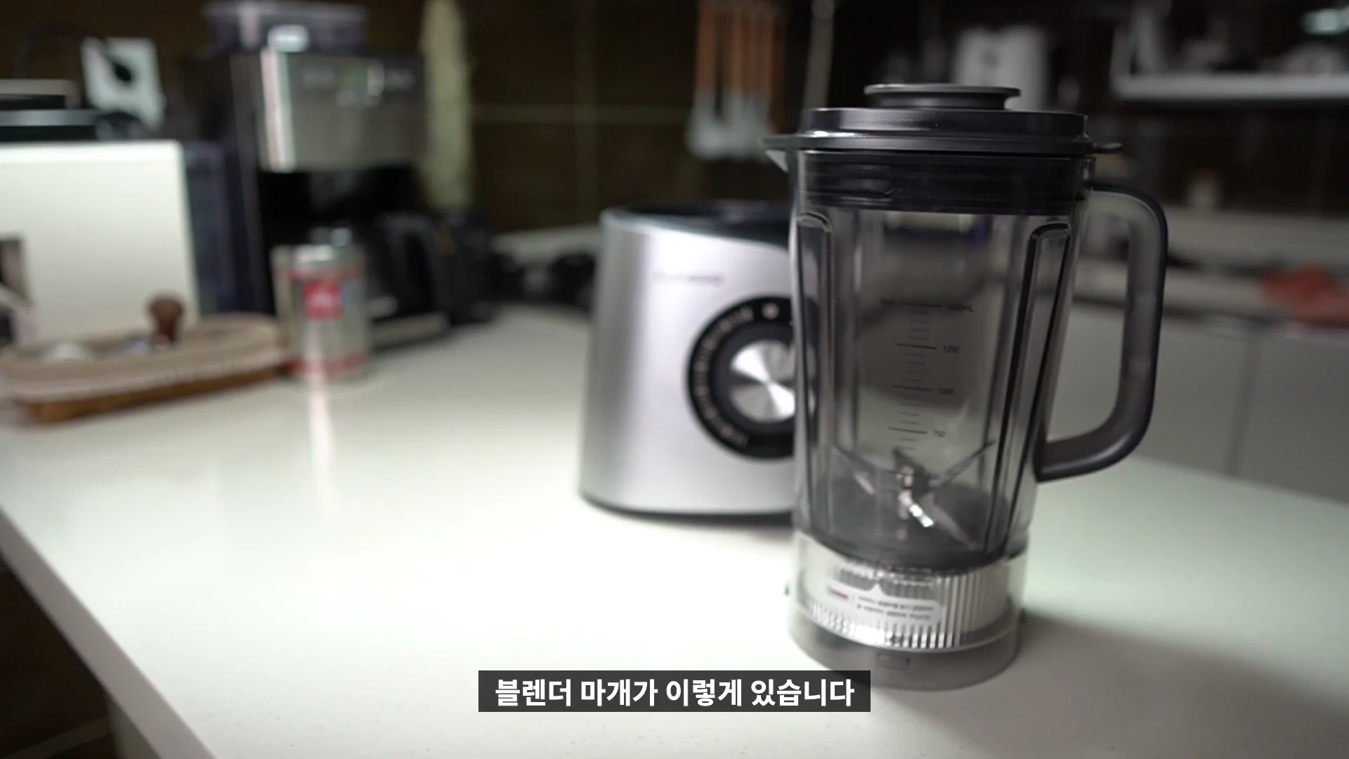 주방 조리대에 놓인 은색 본체와 투명한 용기가 결합된 블렌더