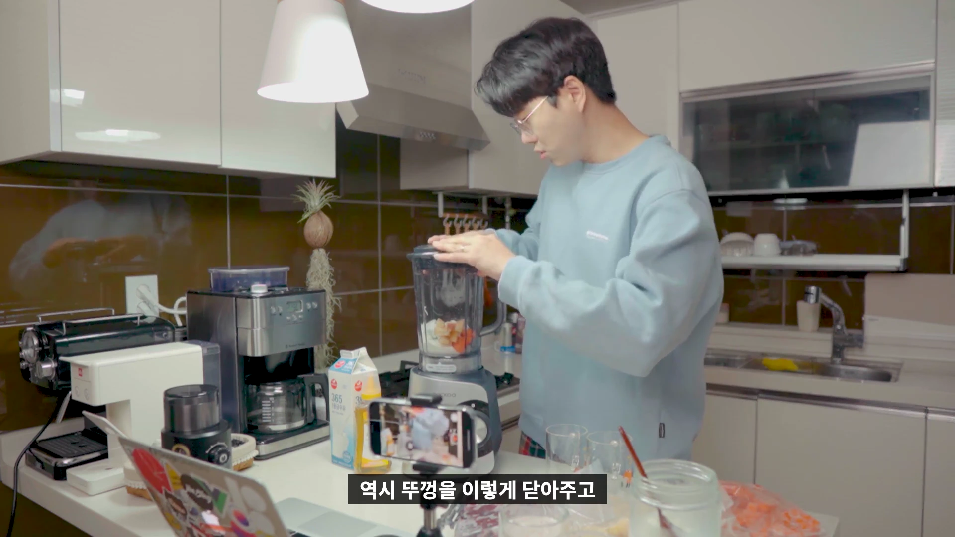 주방에서 안경을 쓴 남성이 블렌더 뚜껑을 닫고 있는 모습