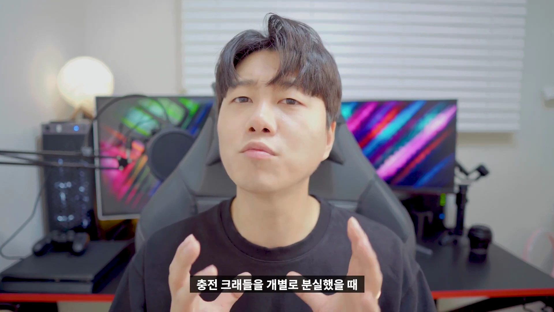 검은색 티셔츠를 입은 남성이 책상 앞에 앉아 손동작을 하며 이야기하는 모습