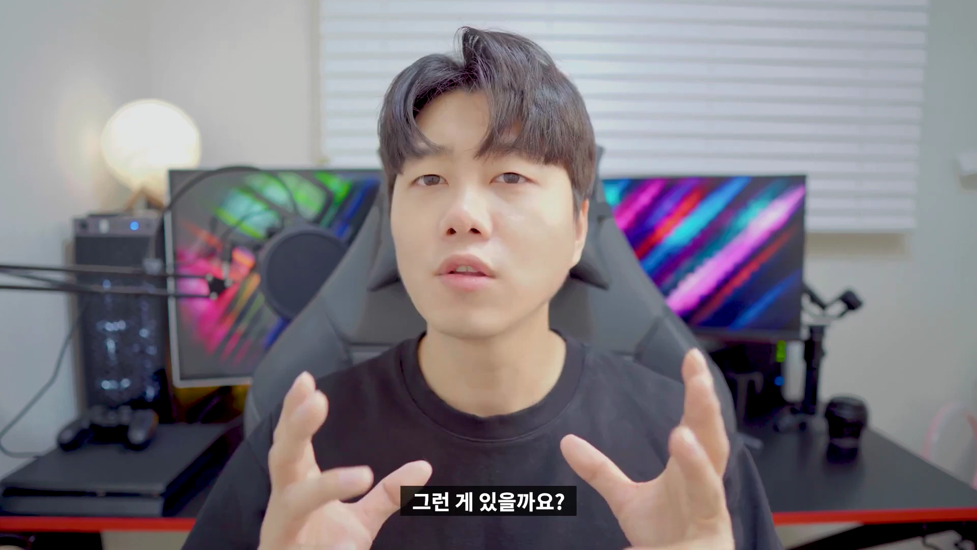 검은색 티셔츠를 입은 남성이 책상 앞에 앉아 손짓하며 이야기하는 모습