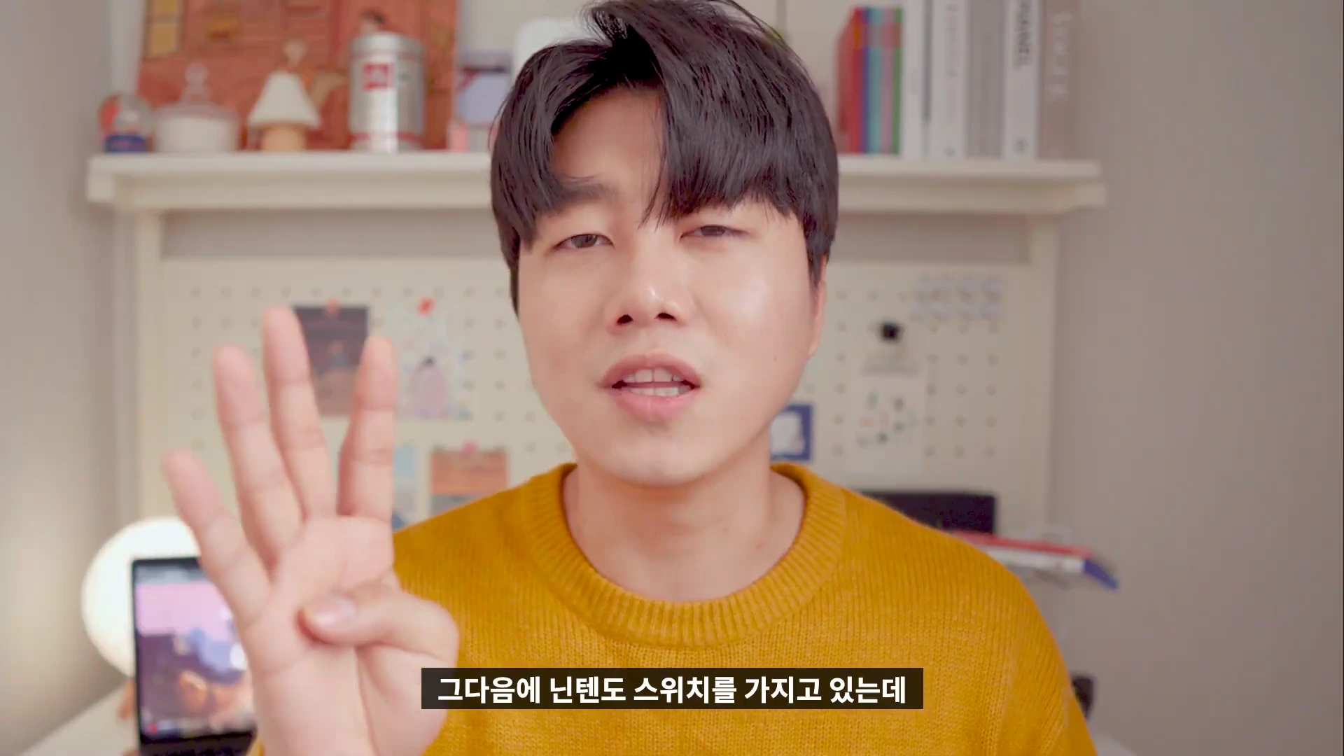 노란색 니트를 입은 남성이 카메라를 보며 손가락으로 숫자 4를 표시하고 있는 모습